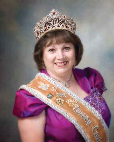 A woman wearing a crown and a sash that says queen
