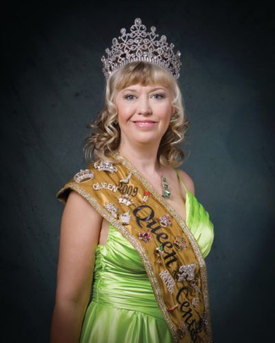 A woman in a green dress is wearing a queen 's sash and tiara