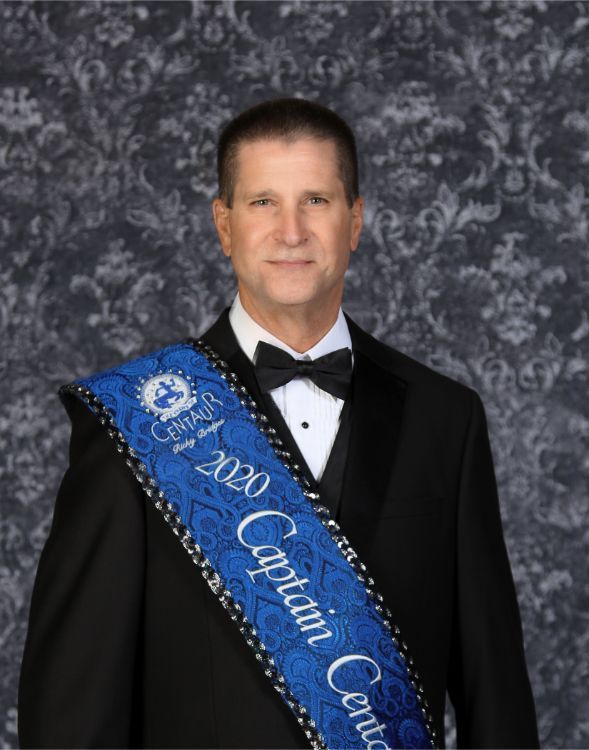 A man in a tuxedo is wearing a sash that says captain center