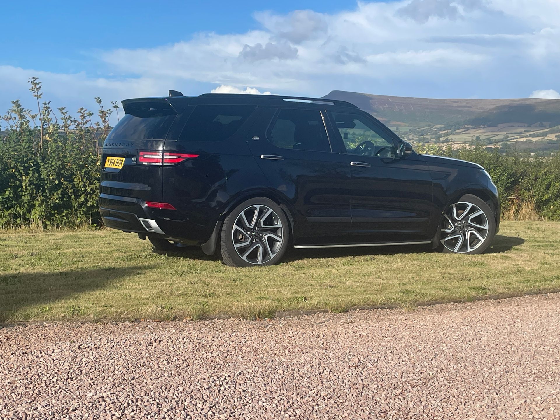 A black Land Rover Discovery parked on a grassy field with a distant mountain landscape in the background.