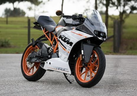 White and orange KTM RC motorcycle on a paved surface, parked with a grassy background.