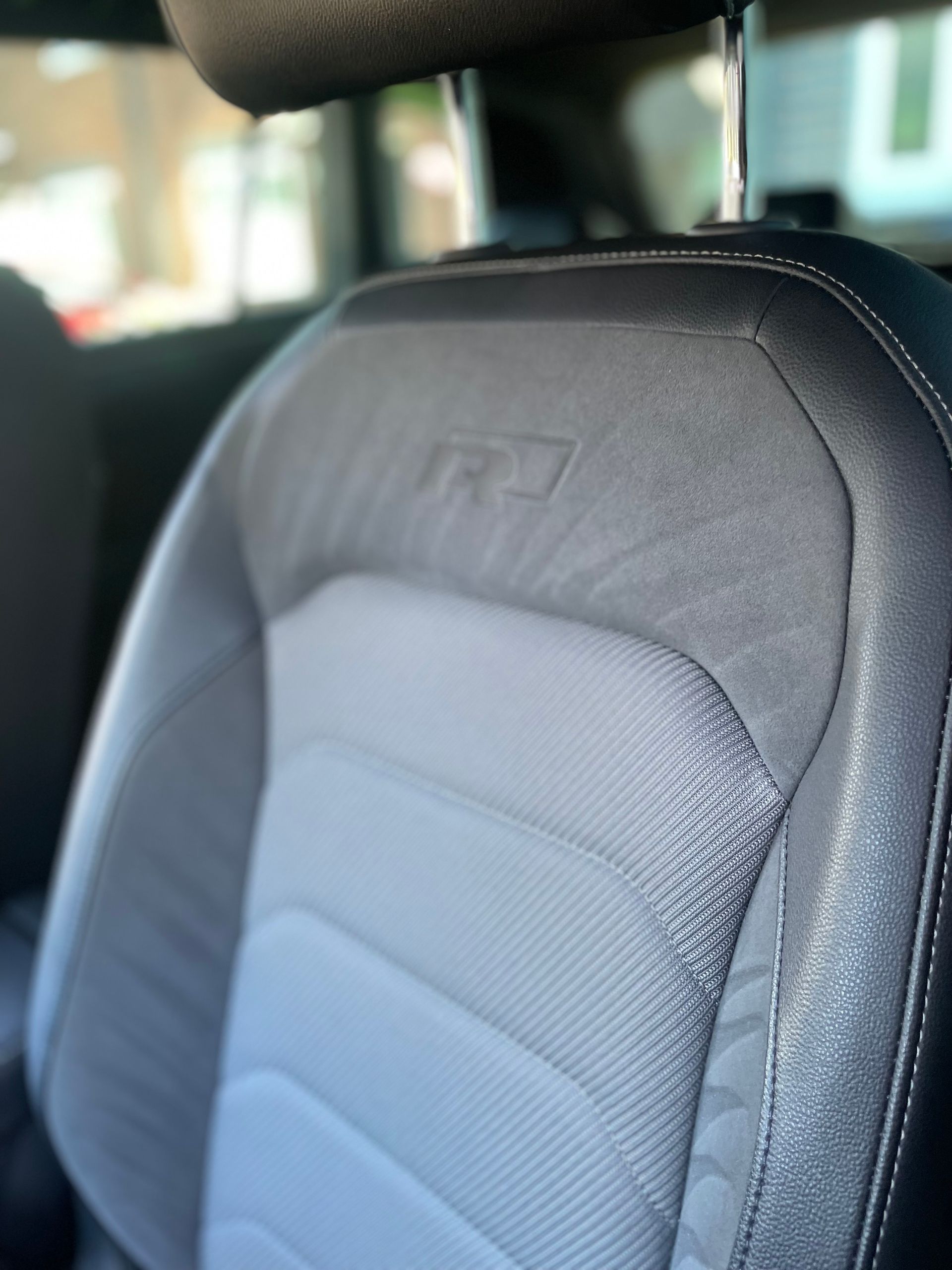 A close-up view of a car seat with a grey fabric center, black side bolsters, and an R-Line logo embossed on the headrest.