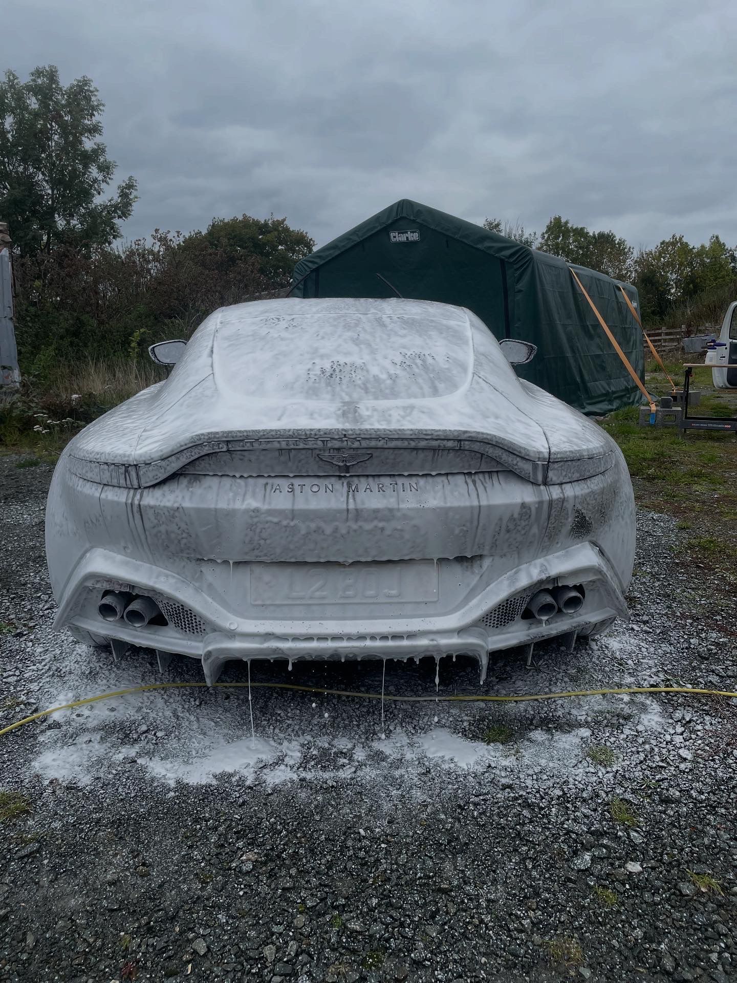 Aston Martin sports car covered in foam suds outdoors, near a tent.