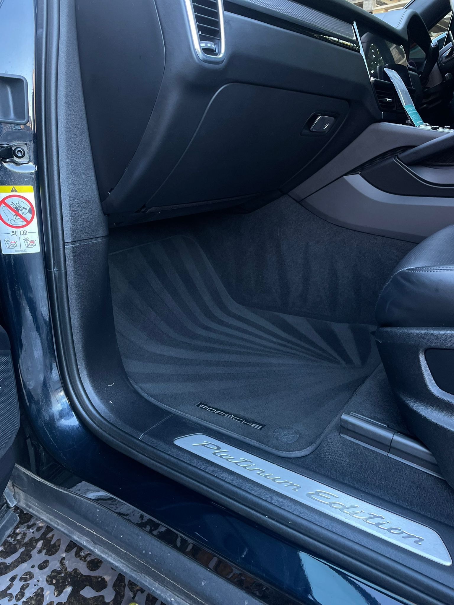 Interior of a dark blue Porsche with floor mat and door sill branding.