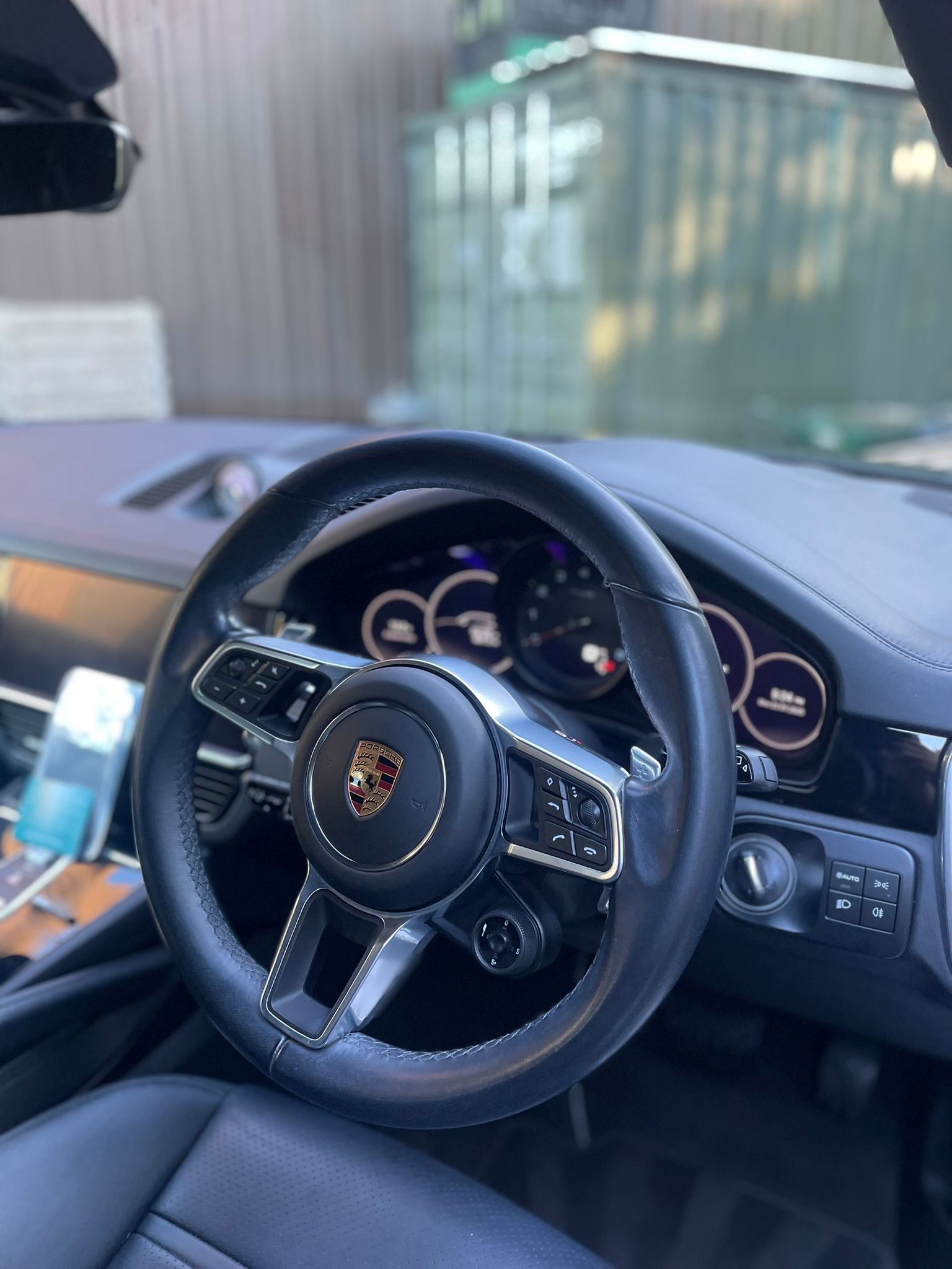 Black leather steering wheel of a Porsche, with silver accents and dashboard visible.