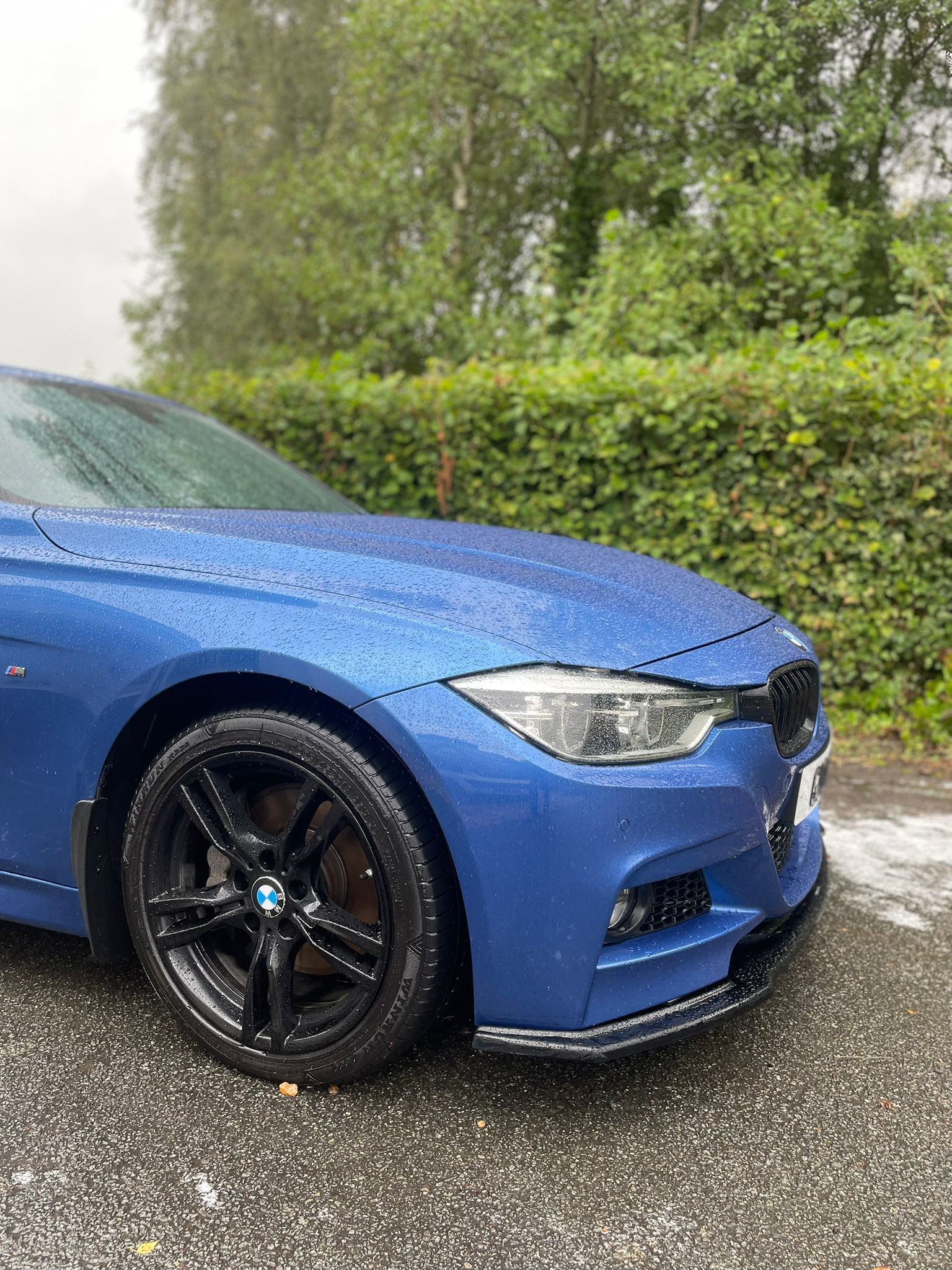 Blue BMW car with black wheels in a rainy outdoor setting.