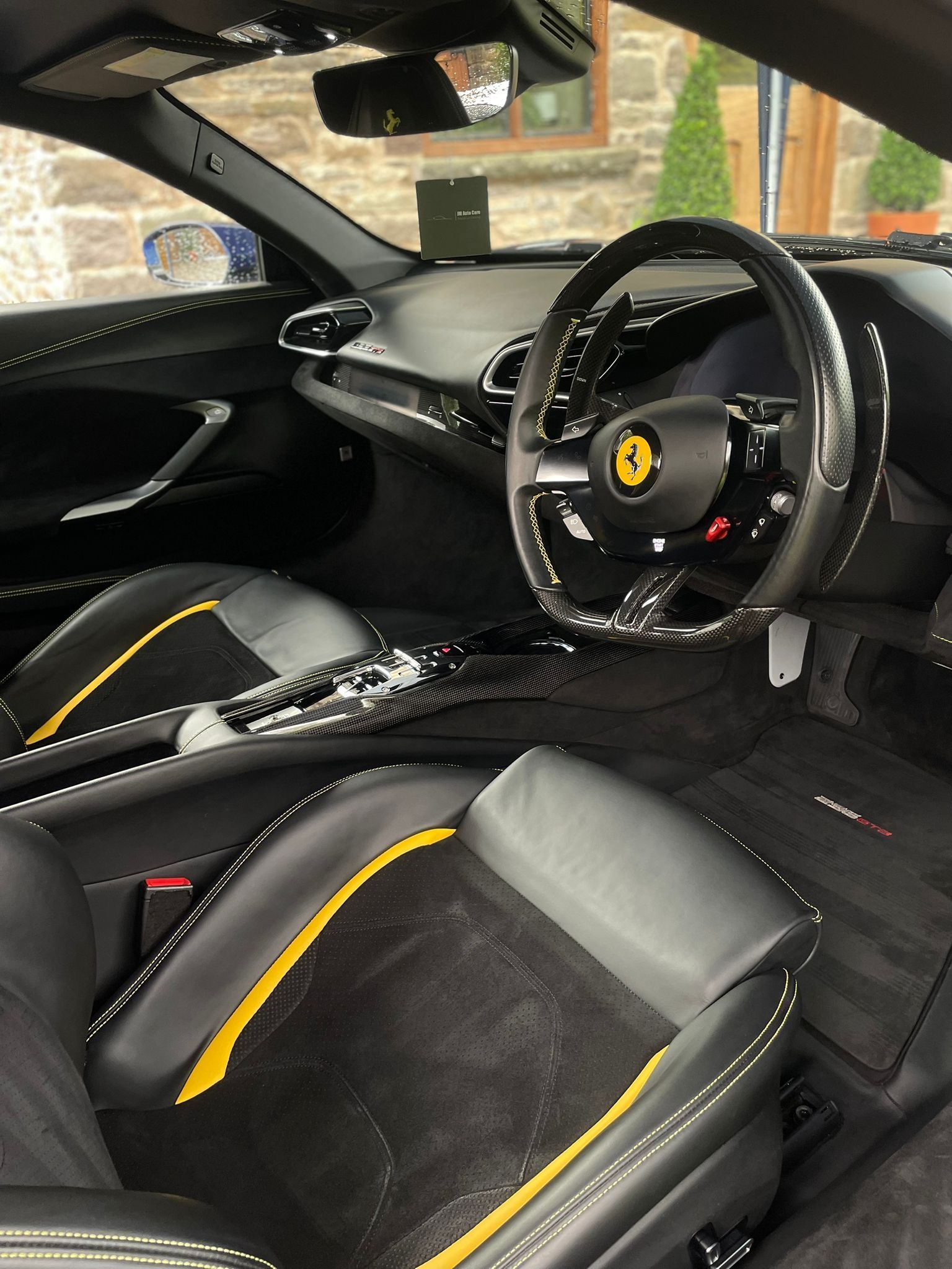 Interior of a black Ferrari with yellow accents and a carbon fiber steering wheel.