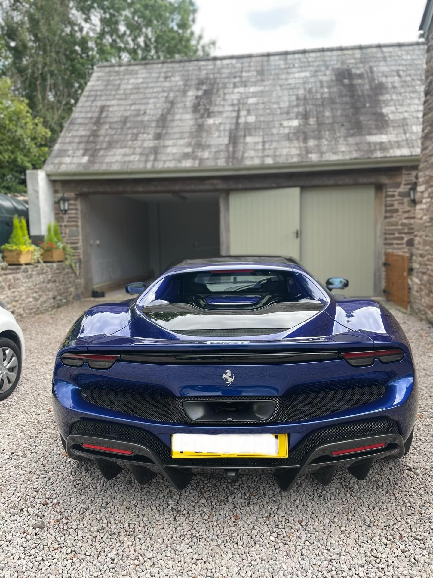 Blue Ferrari parked in front of a stone garage, on a gravel driveway.