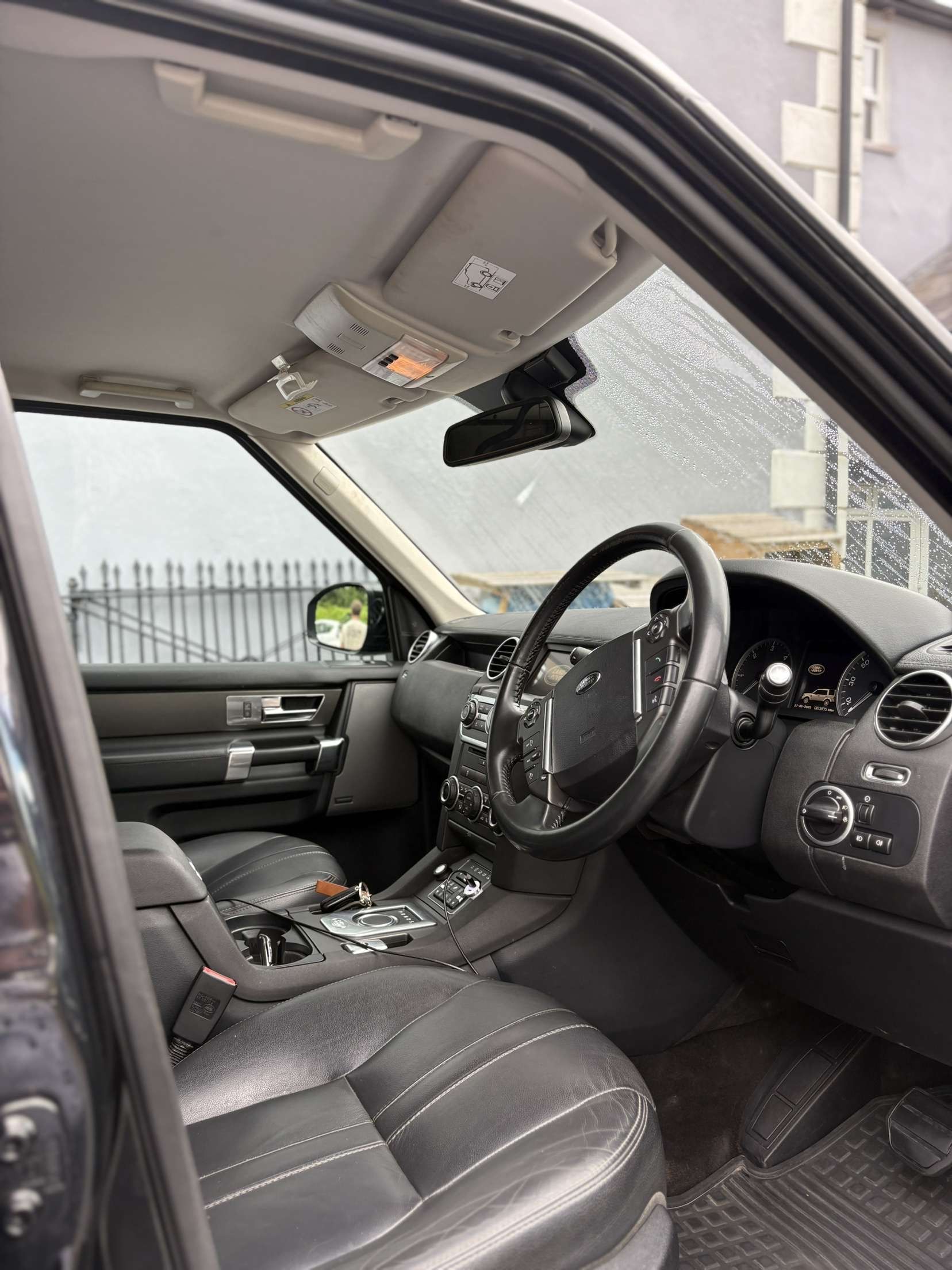 Interior view of a vehicle showing black leather seats, a steering wheel, and a center console from the driver's side door.