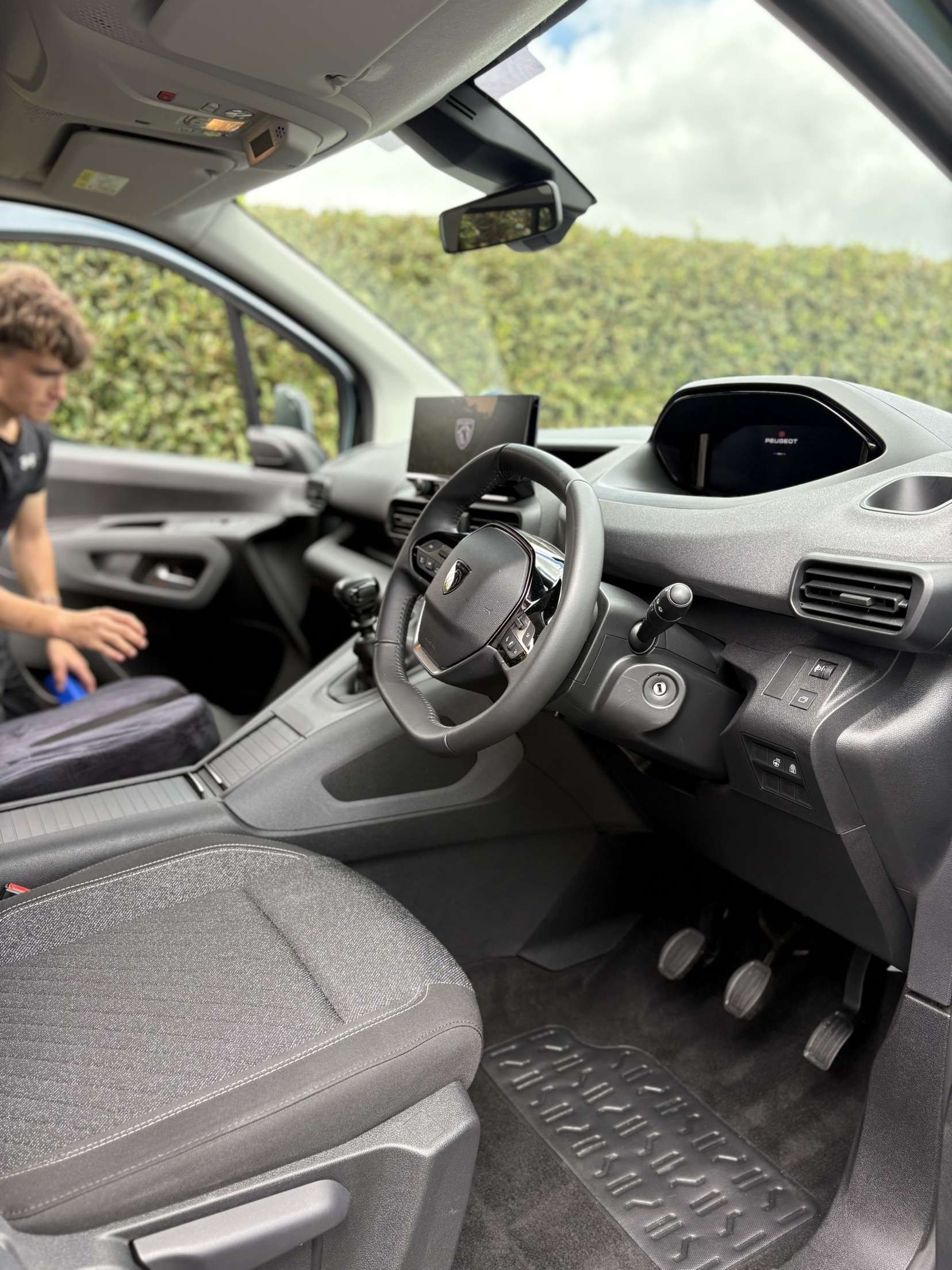 Interior of a vehicle from the driver's side, showing a steering wheel, digital dashboard, and patterned seats.