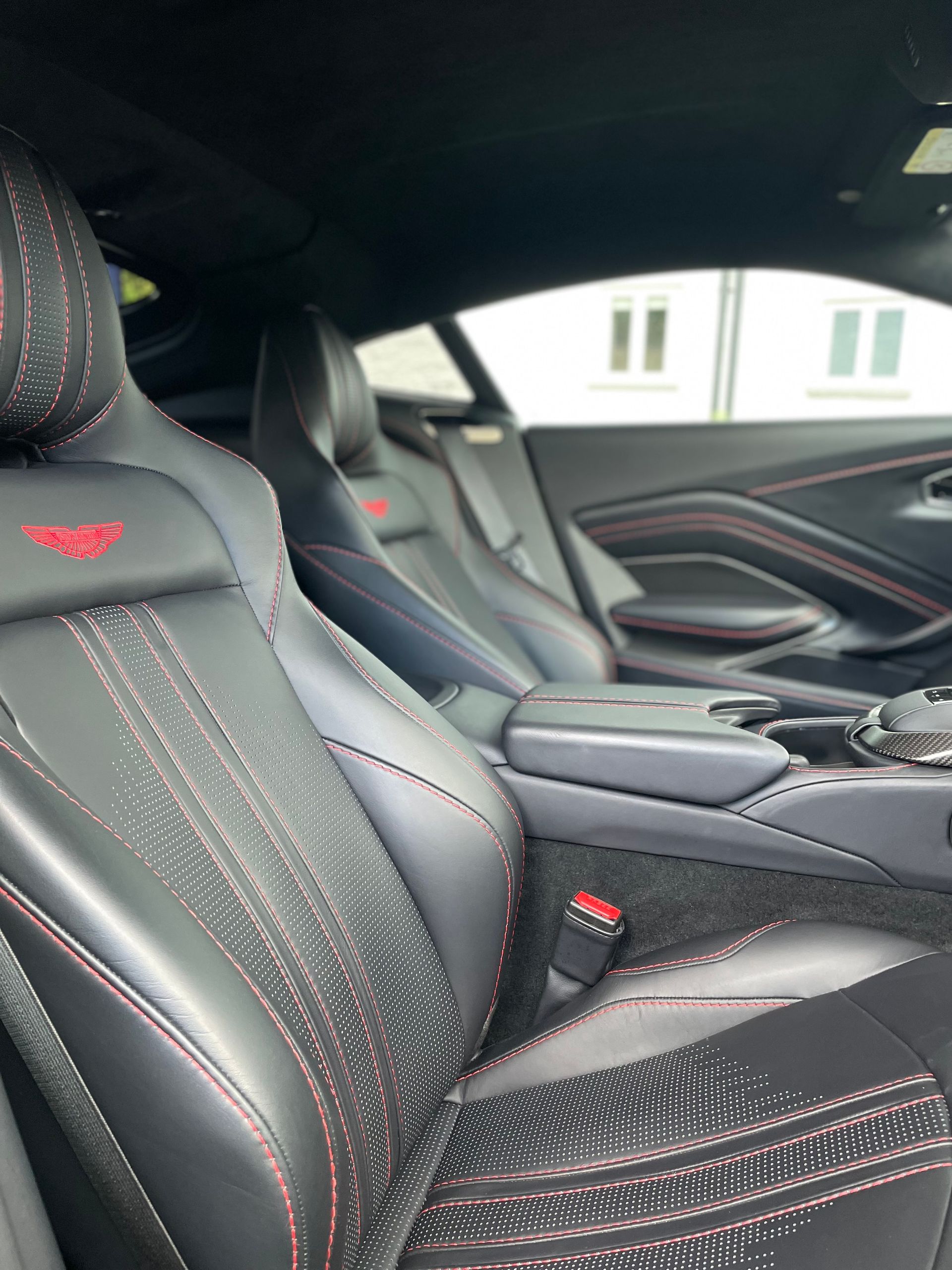 Car interior featuring black leather seats with red stitching and a red embroidered logo, viewed from the driver's side.
