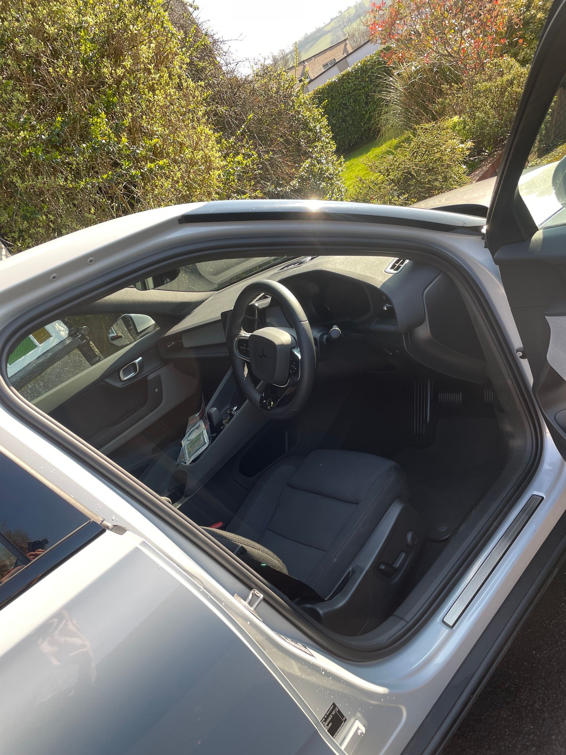 Interior of a silver car with a black steering wheel and dark upholstery, captured through the open driver-side door.