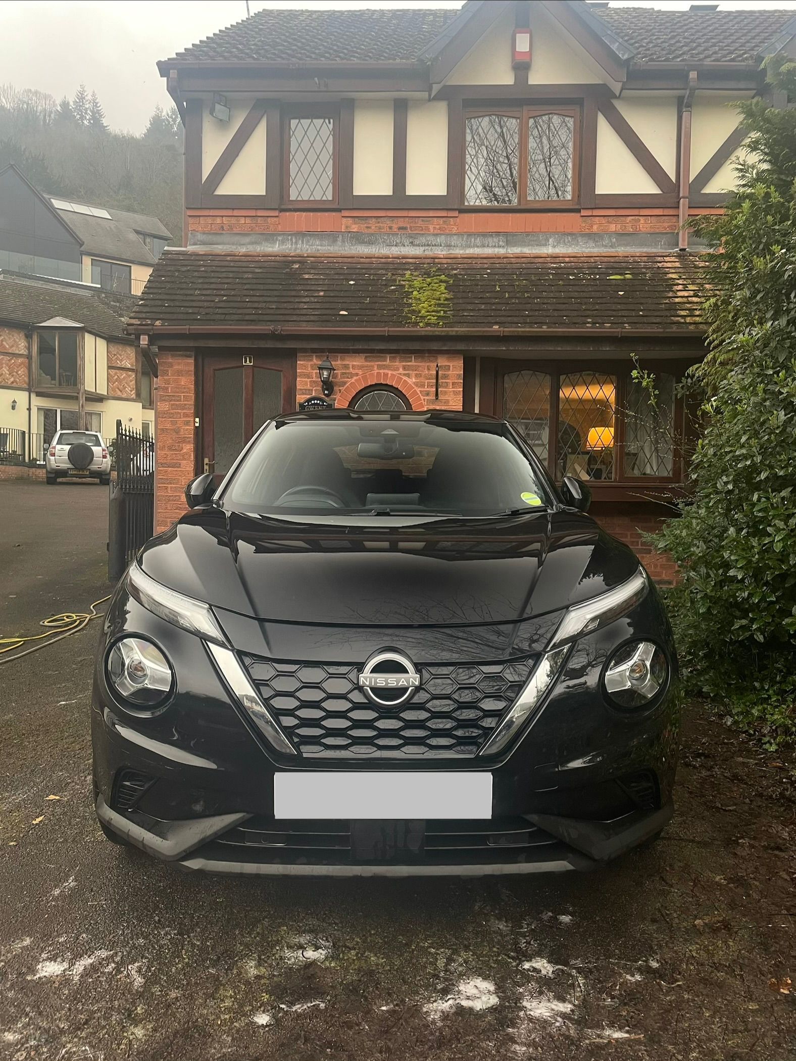 A black Nissan Juke parked in front of a house with a Tudor-style brick and timber facade.