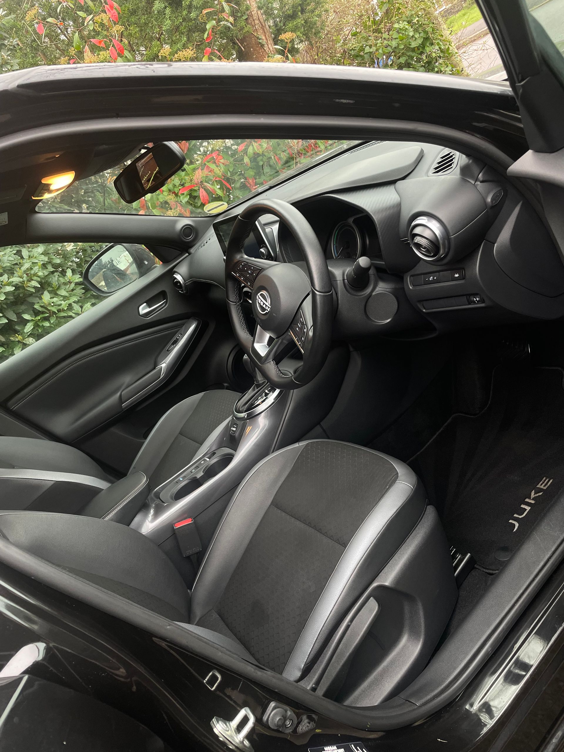 Interior of a black Nissan Juke, showing the steering wheel, dashboard, and cloth-upholstered front seats.