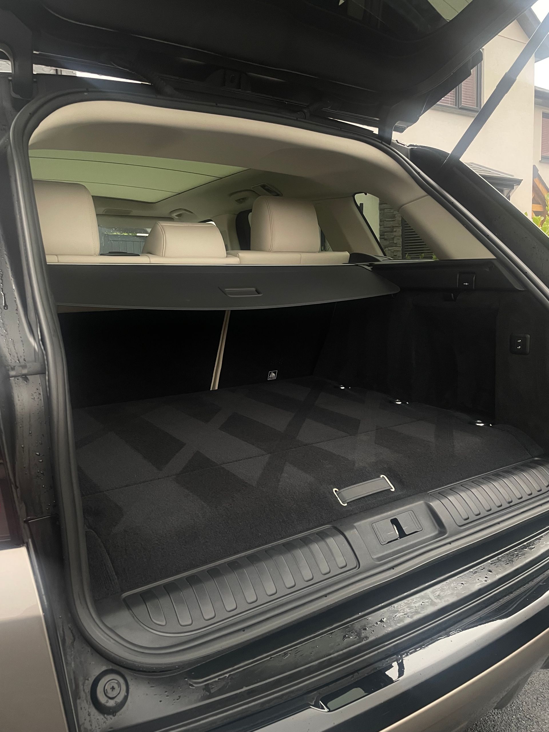 Open trunk of an SUV with cream-colored seats, a retractable cargo cover, and a black patterned floor mat.