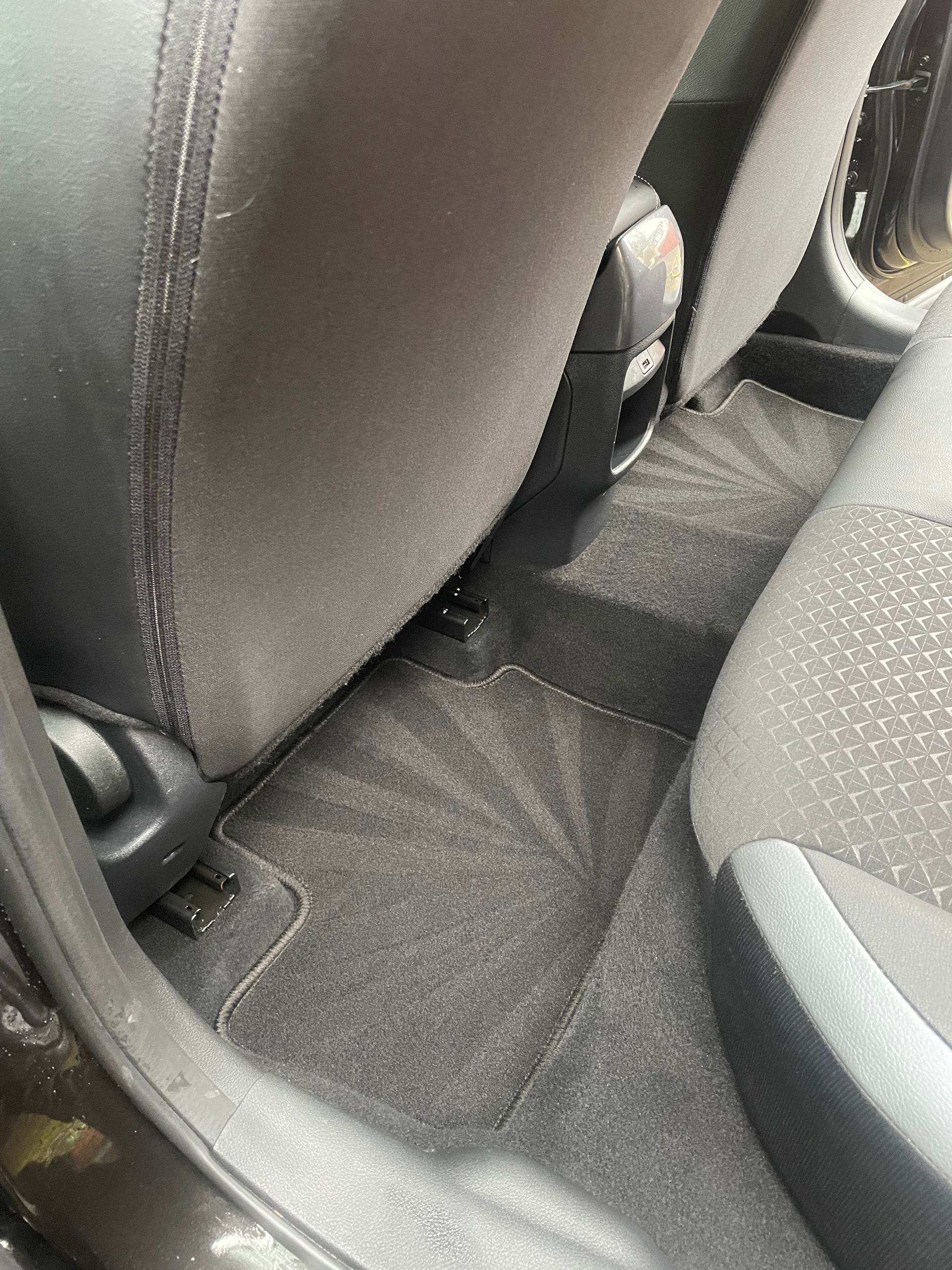 The rear footwell of a car featuring clean, dark gray carpet and fabric seats.