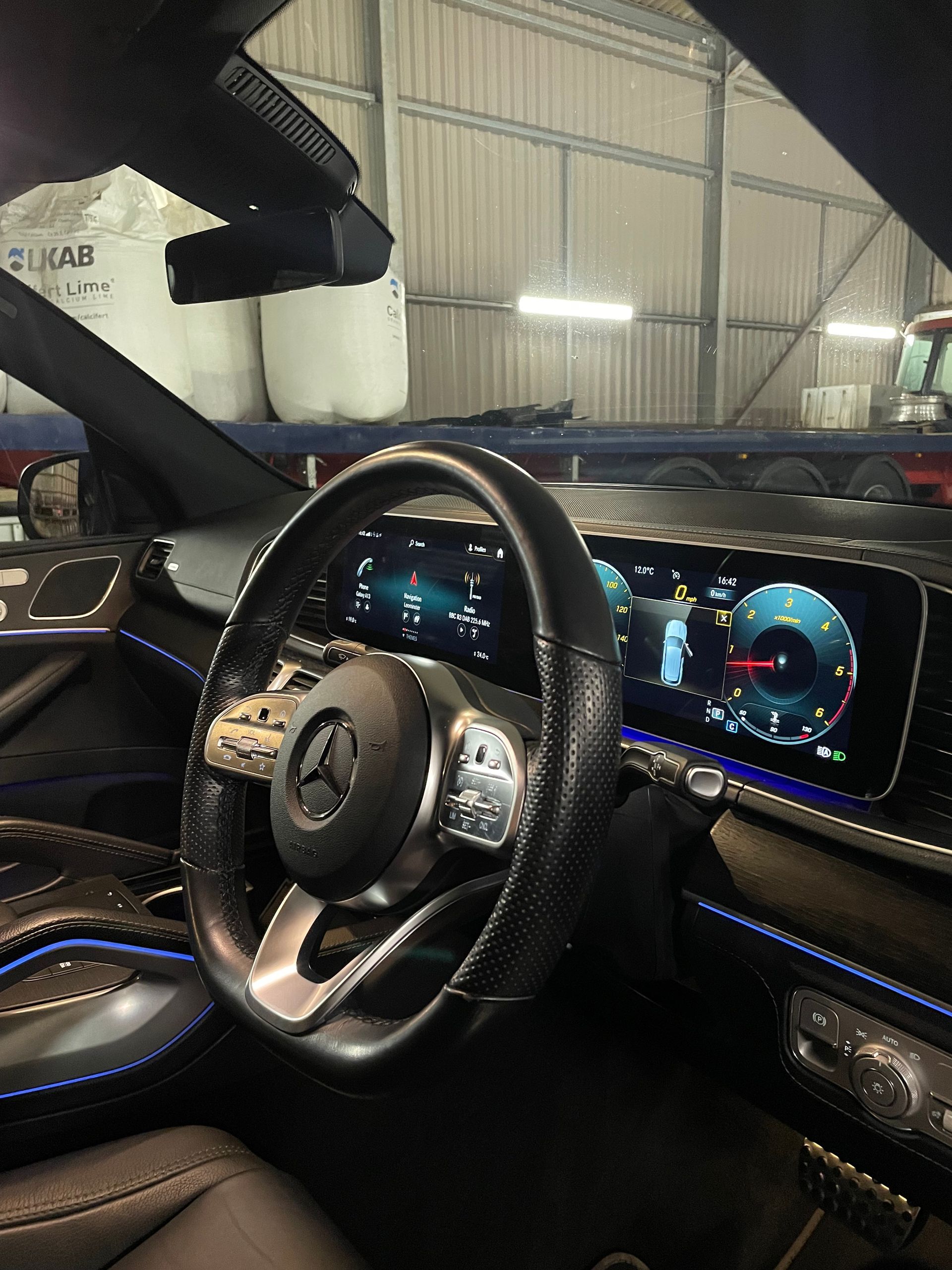 Interior view of a modern Mercedes-Benz driver seat with a digital dashboard and illuminated blue accent lighting.