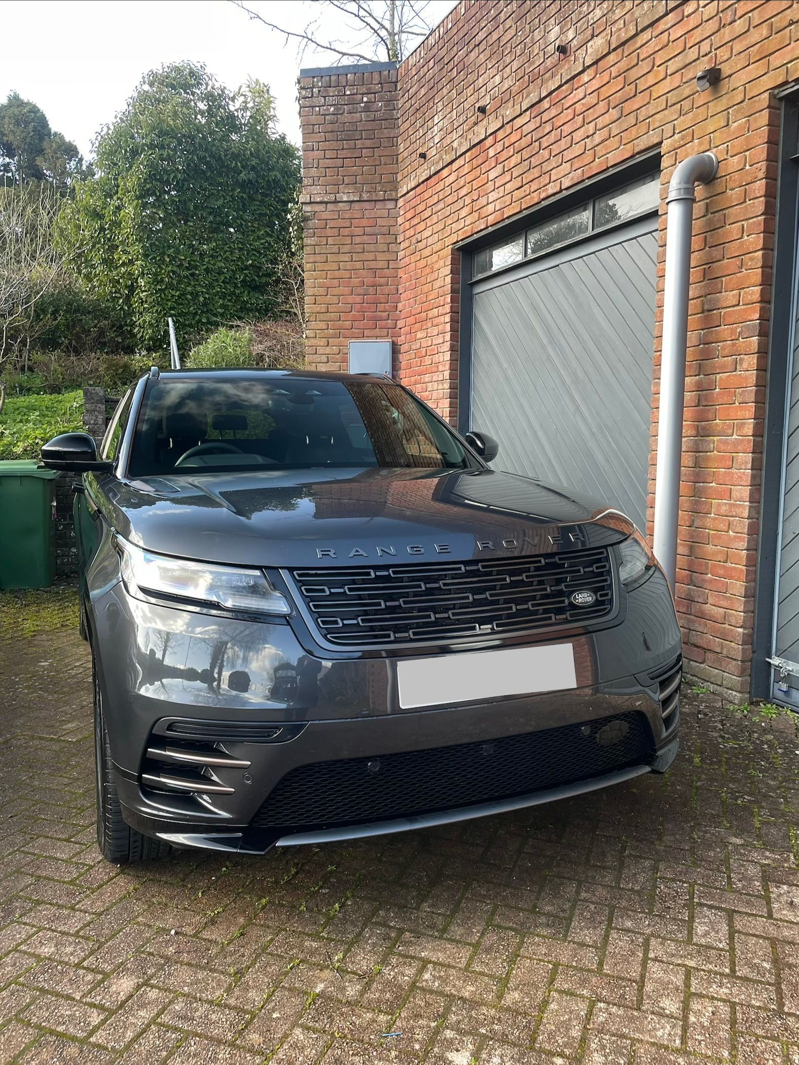 A dark gray Range Rover Velar parked on a paved driveway in front of a brick building.