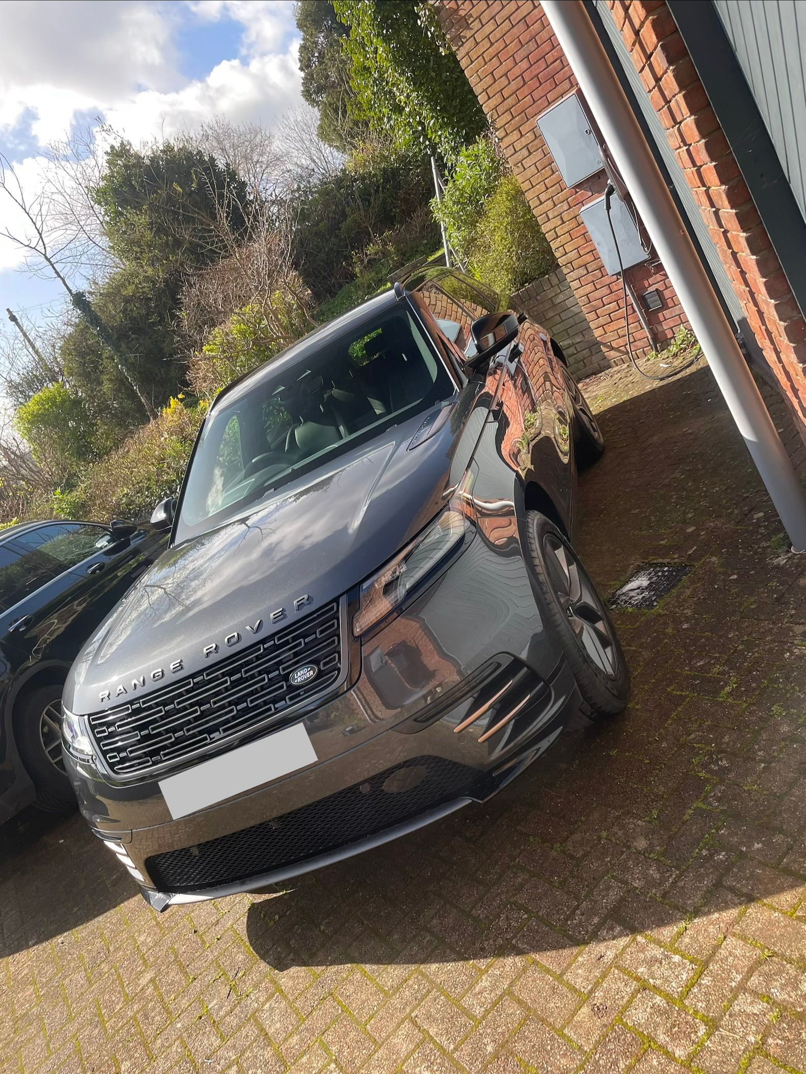 A dark grey Range Rover parked on a brick driveway near a brick building.