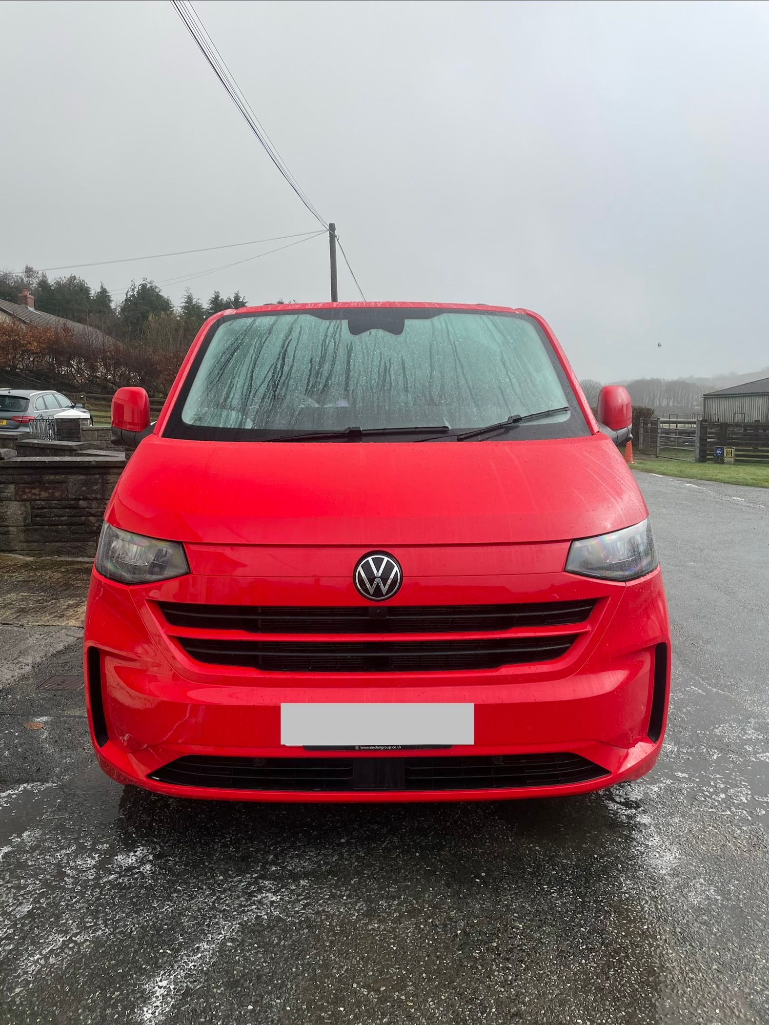 A bright red Volkswagen Transporter van parked outdoors on a grey, overcast day.
