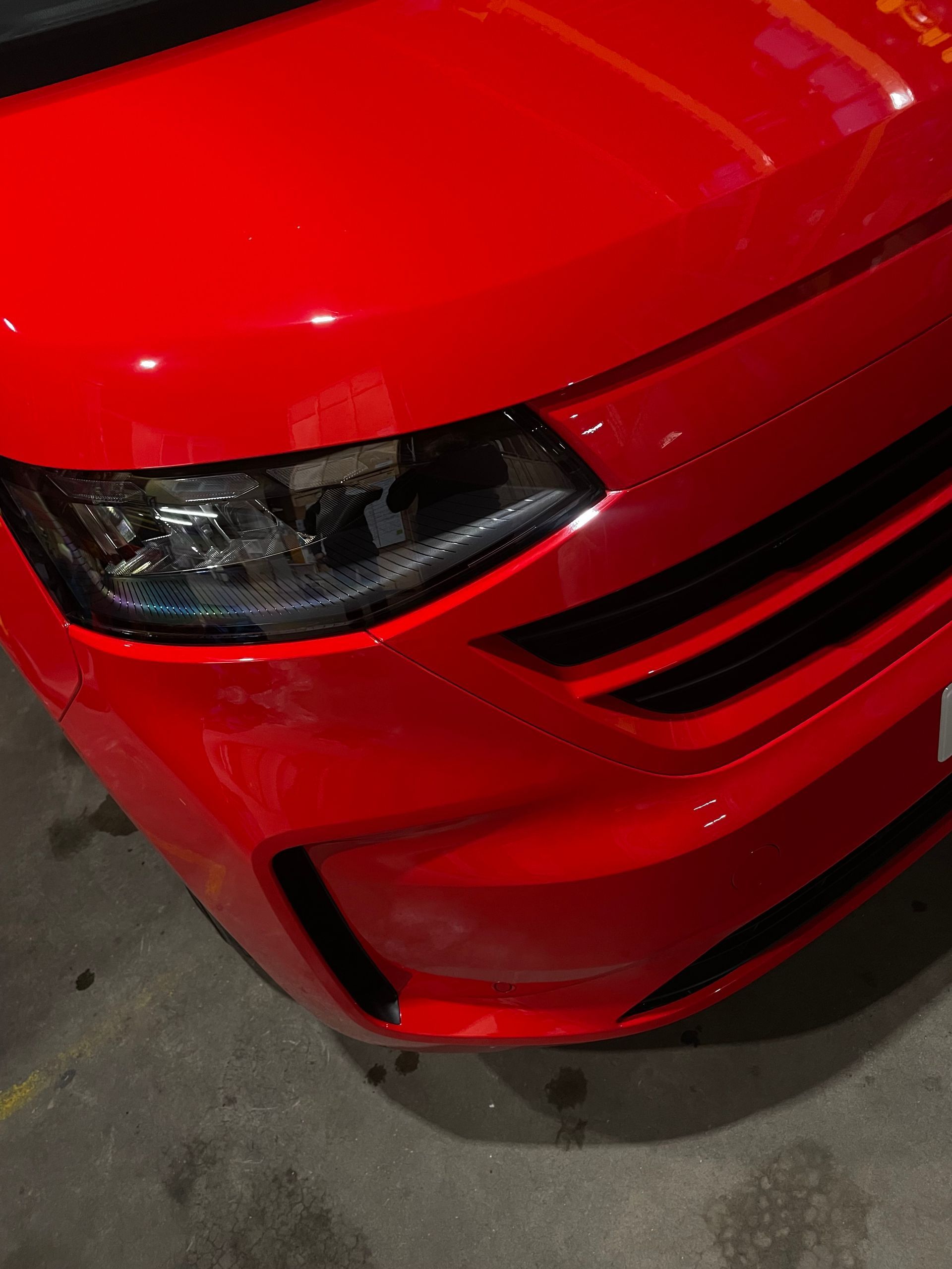 Close-up view of the front driver-side corner of a bright red car, focusing on the headlight and bumper.