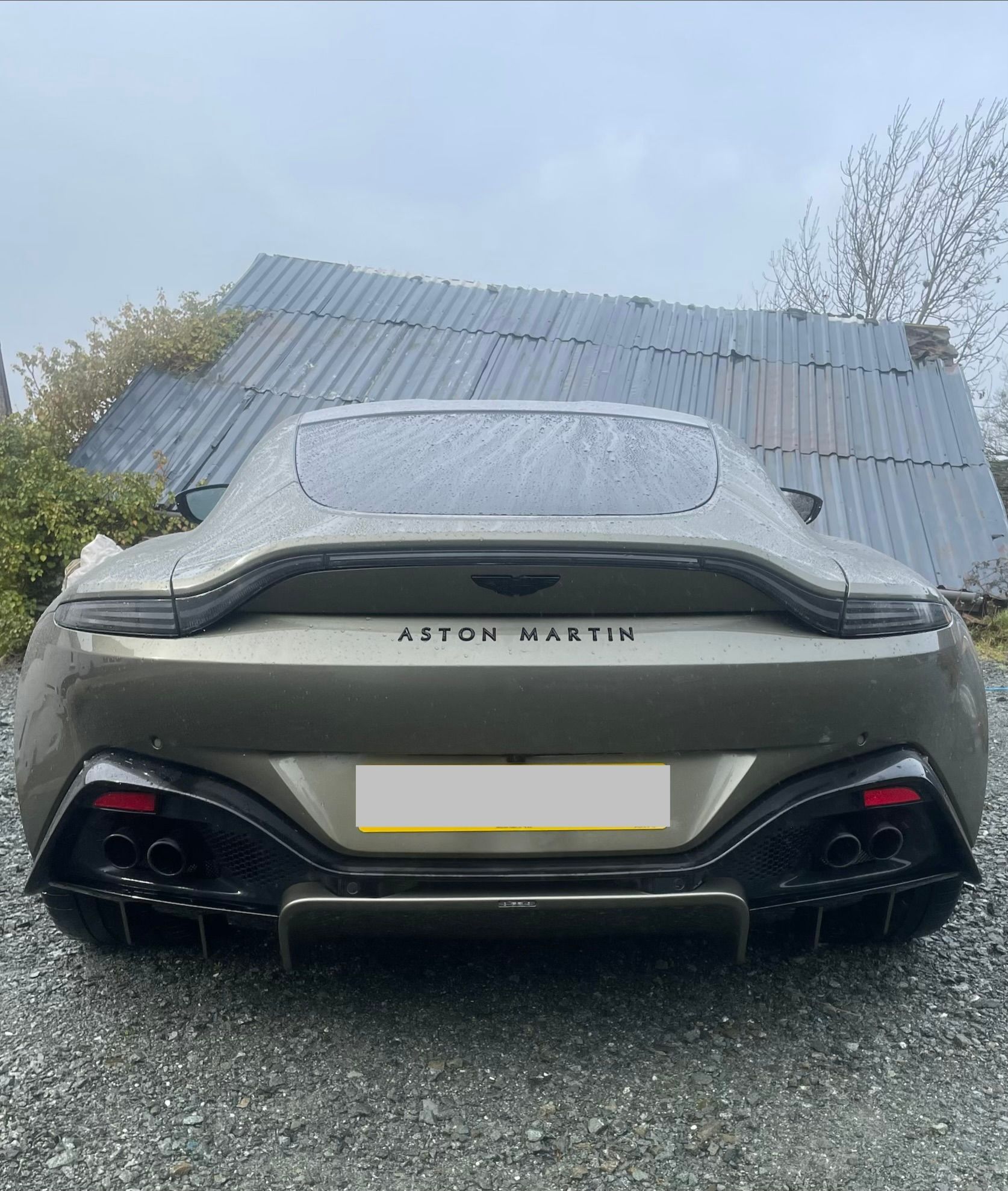 A metallic taupe Aston Martin Vantage viewed from the rear, featuring a carbon fiber diffuser and quad exhaust pipes.