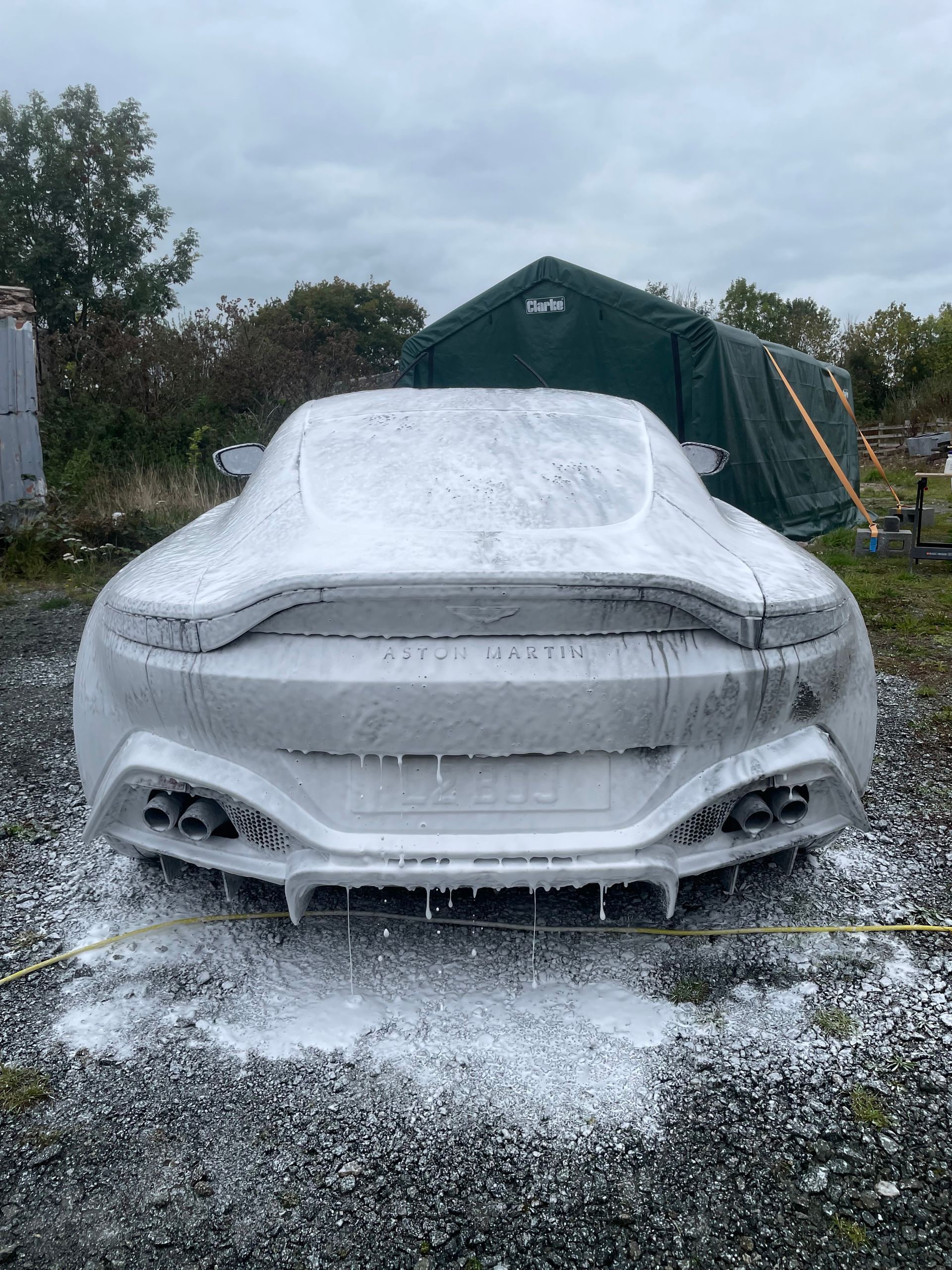 Aston Martin car covered in white foam, being washed outdoors.