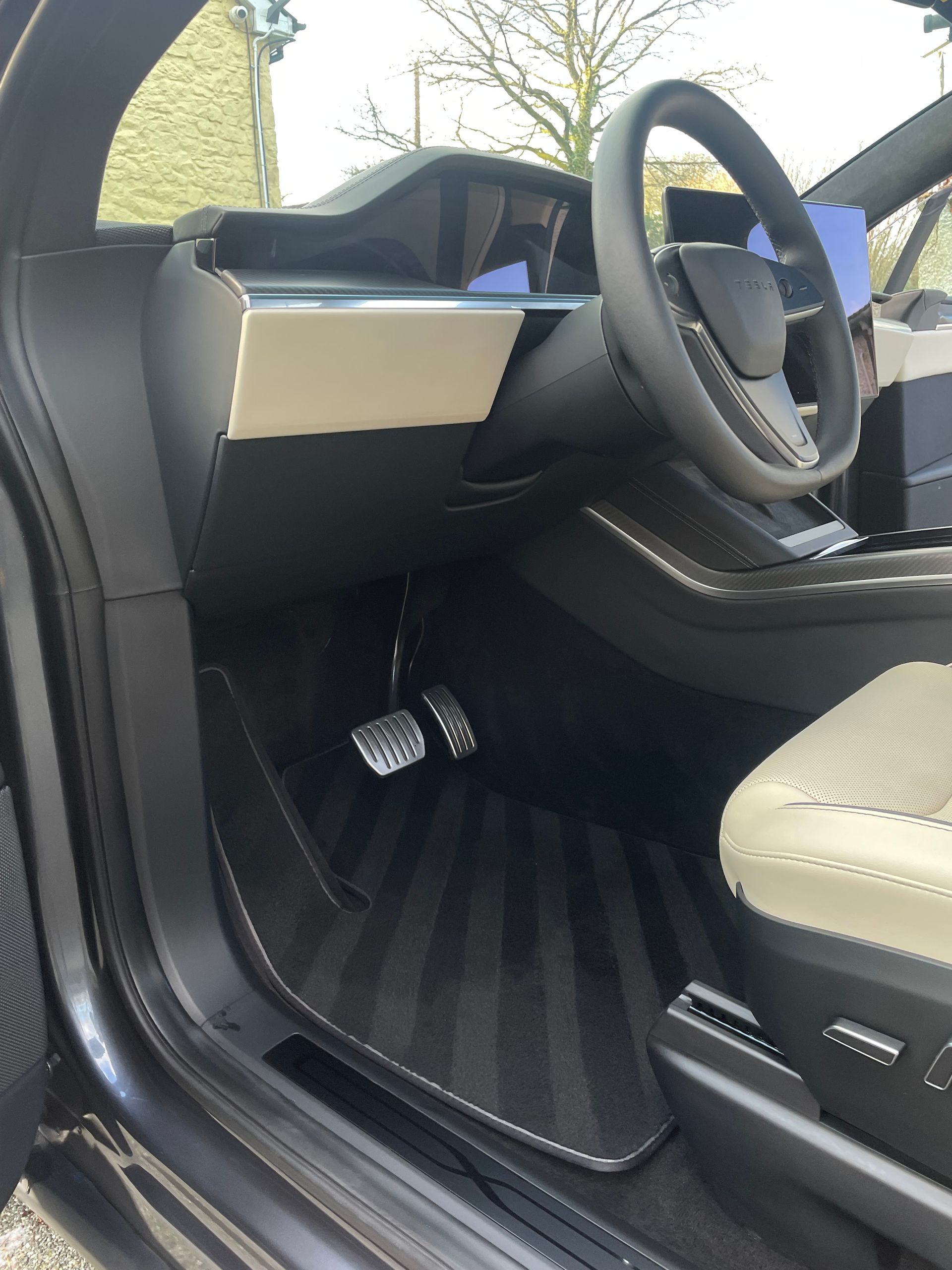 The interior of a vehicle featuring a dark steering wheel, a cream-colored dashboard accent, and textured floor mats.