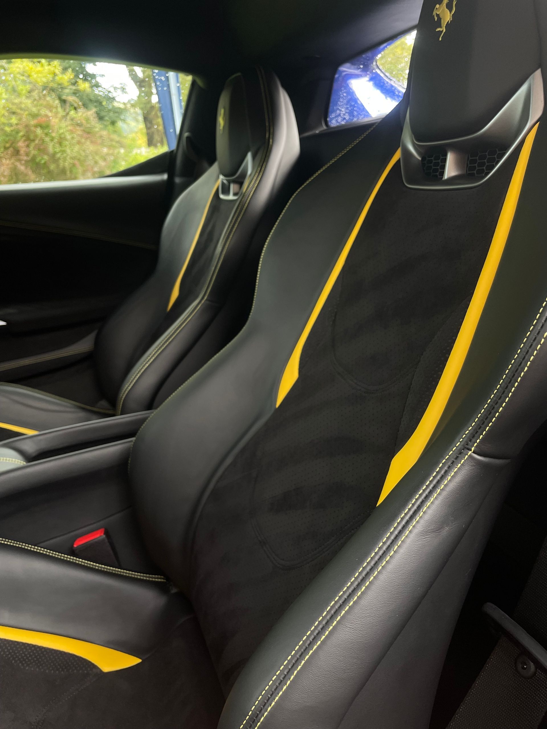 Interior view of a luxury car with black leather racing seats, yellow accents, and Ferrari logos on the headrests.