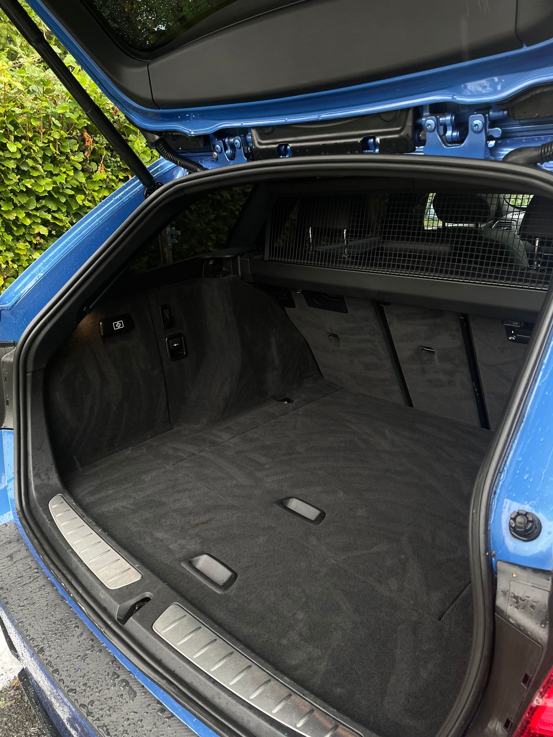 The open trunk of a blue vehicle, showing a spacious, carpeted interior with a cargo cover and side compartments.