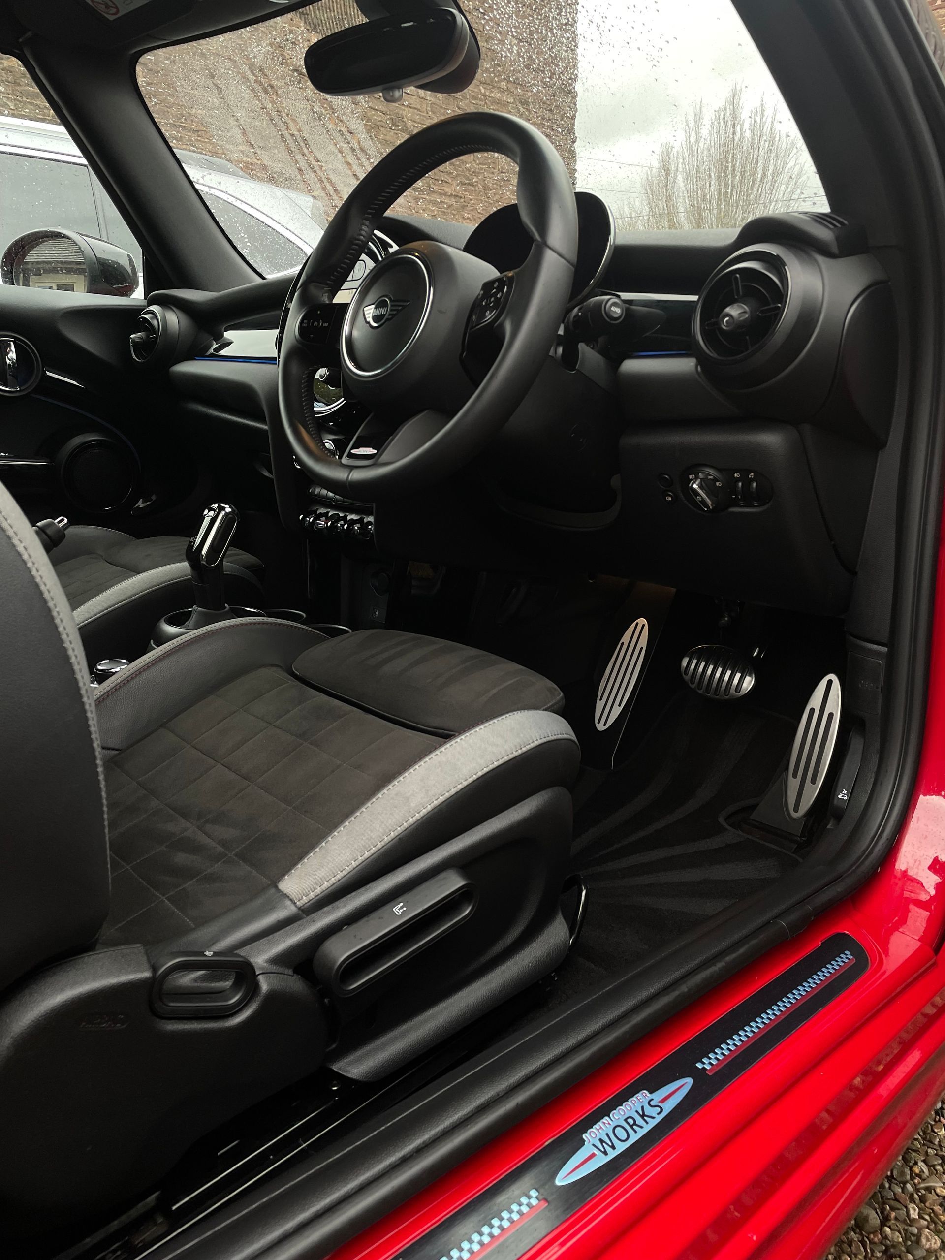 Interior of a red car showing the steering wheel, driver’s seat, and pedal area.
