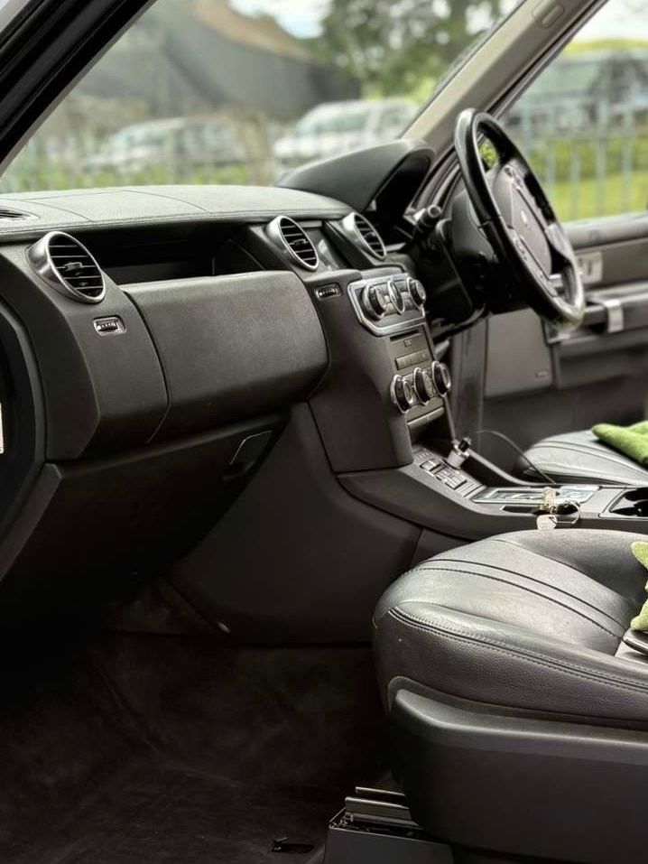 The driver's side interior of a black car featuring leather seats, a dashboard with air vents, and a steering wheel.