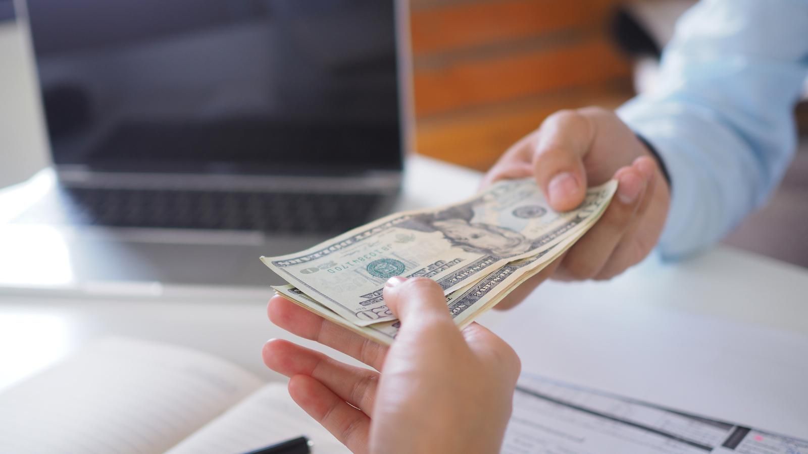 A person is paying off a loan with a stack of money to a teller.