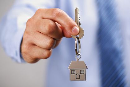 Caption Holding out house keys on a house shaped keychain