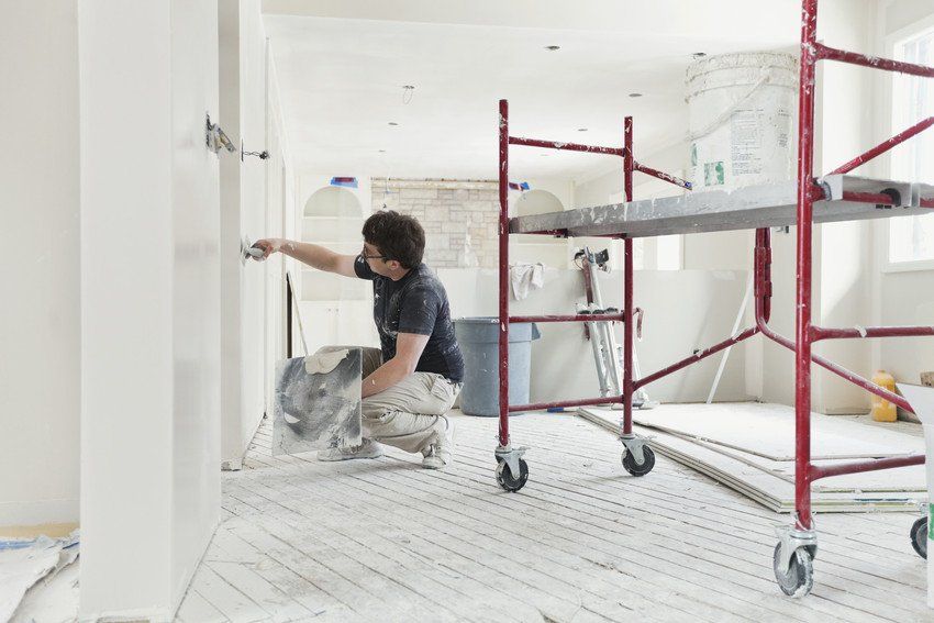 Tradesman plastering drywall with trowel in home