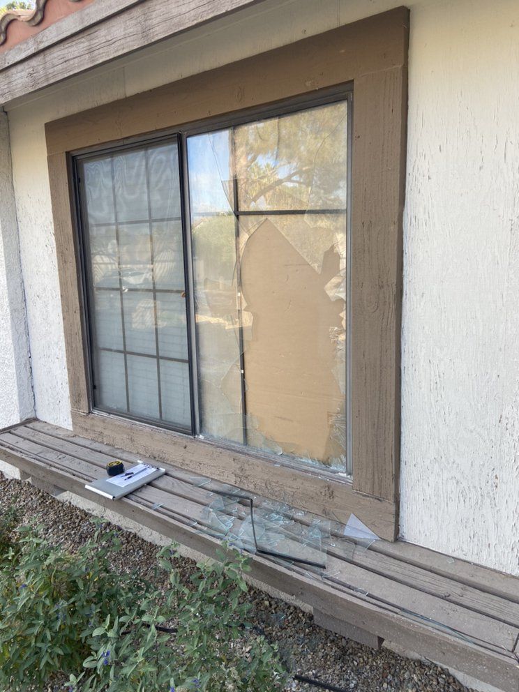 Broken window, glass shards below, patched with cardboard. Exterior of a home.