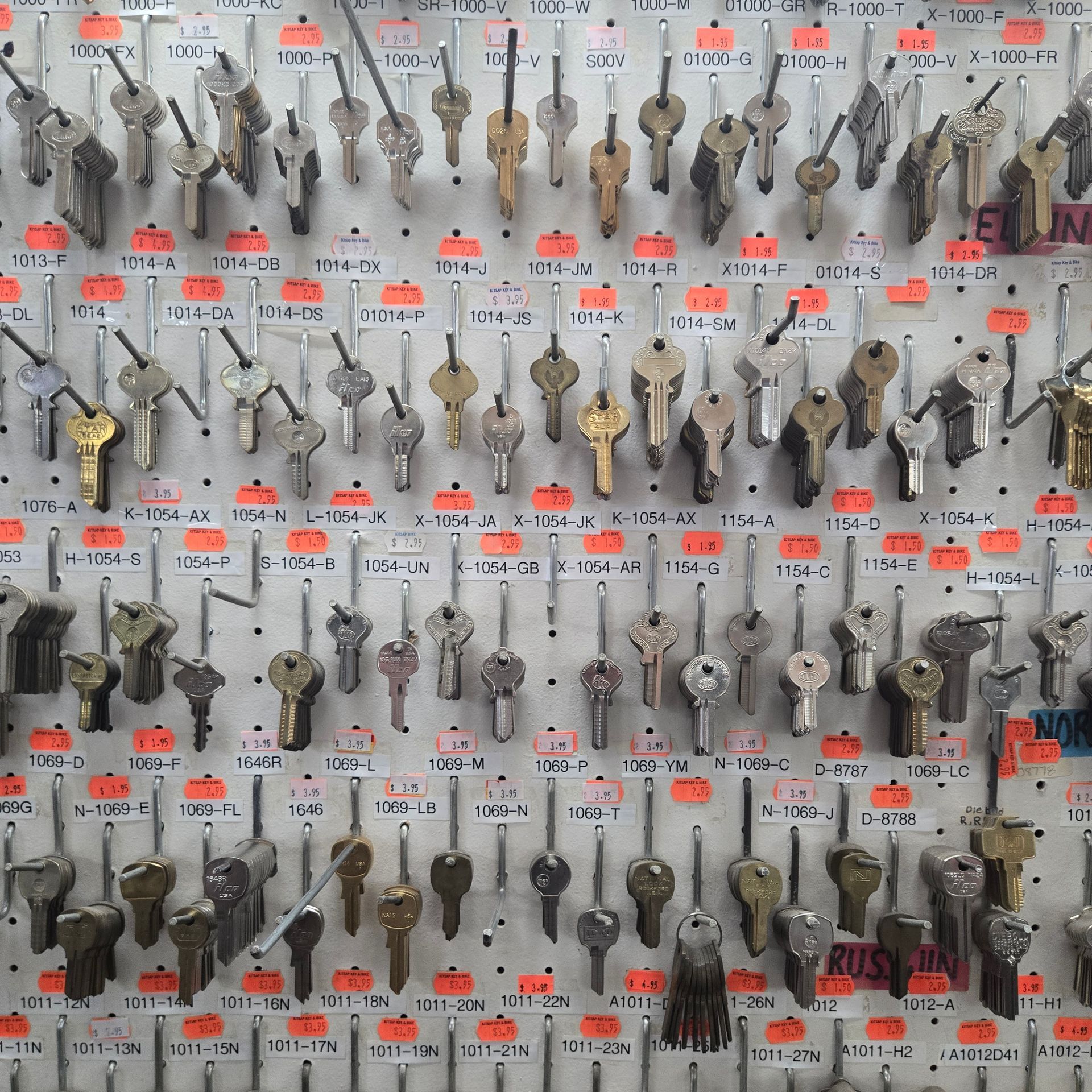 A bunch of keys are hanging on a wall including one that says ' ross ' on it