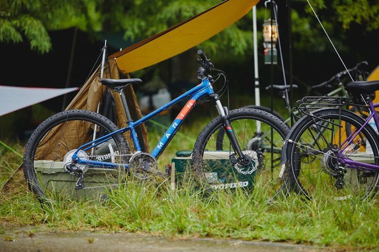 Two bicycles are parked next to each other in the grass in front of a tent.