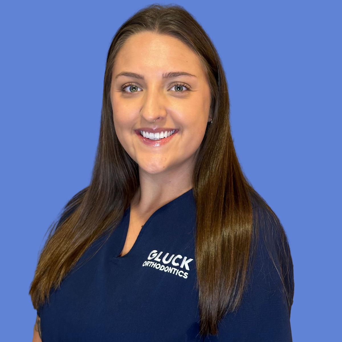 A woman in a black scrub top is smiling in front of a blue background that says gluck