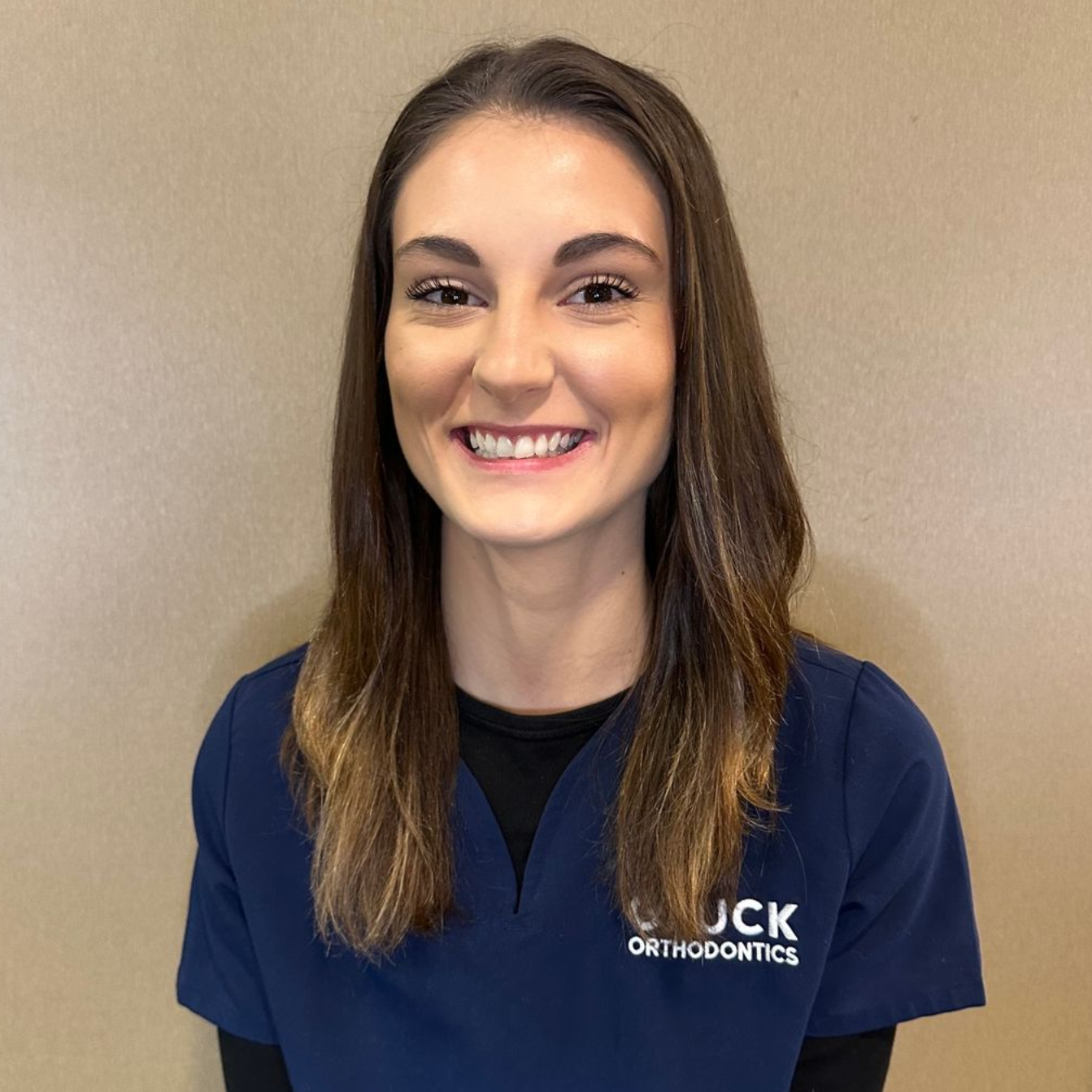 Smiling woman in navy polo standing against a beige wall