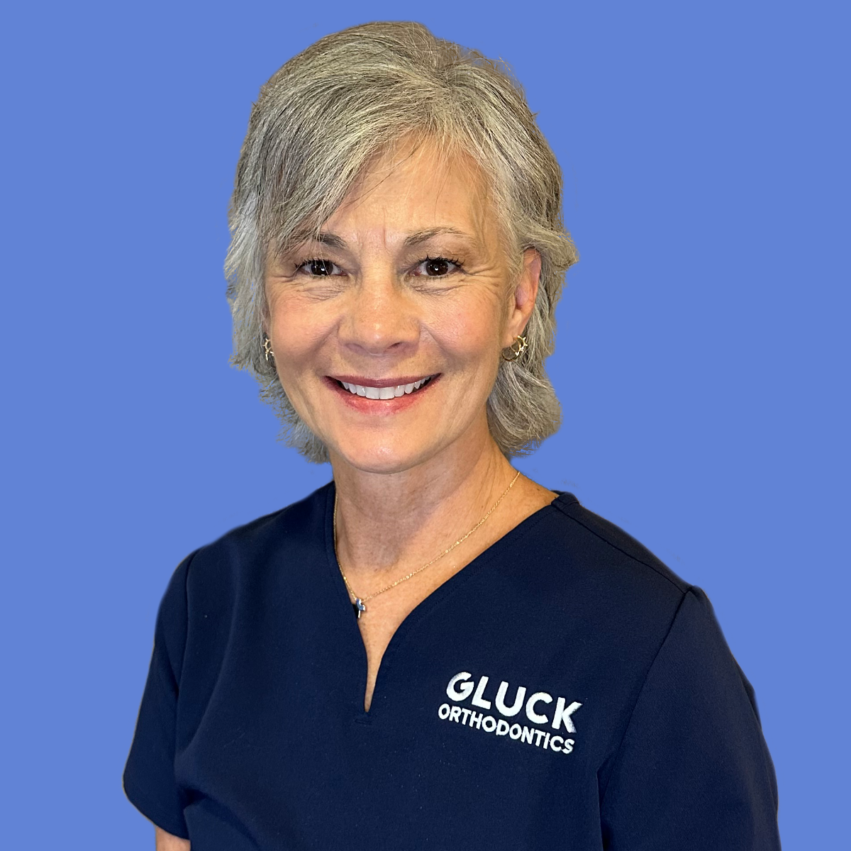 A woman in a black jacket is smiling in front of a blue wall with the word gluck on it.