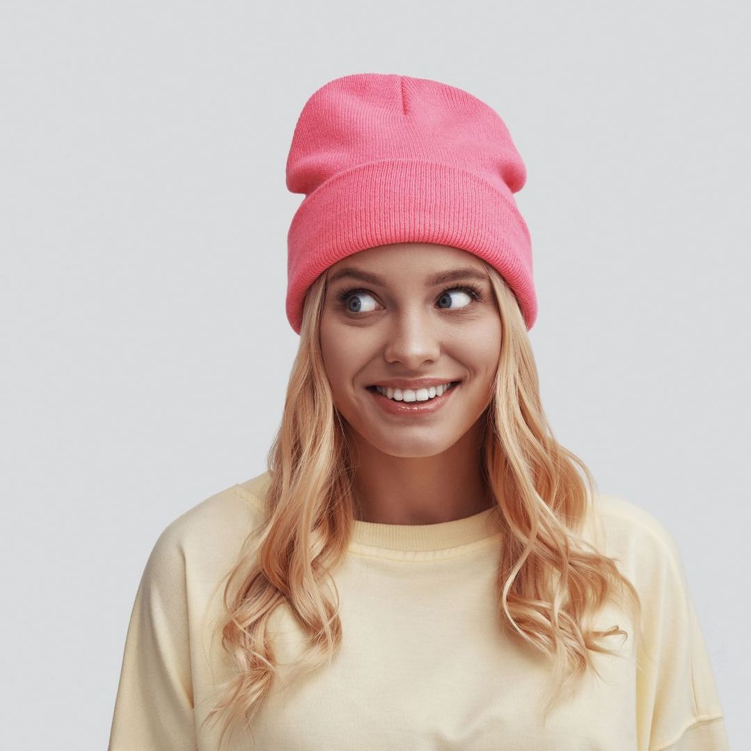 A woman wearing a pink beanie and a yellow sweater is smiling.