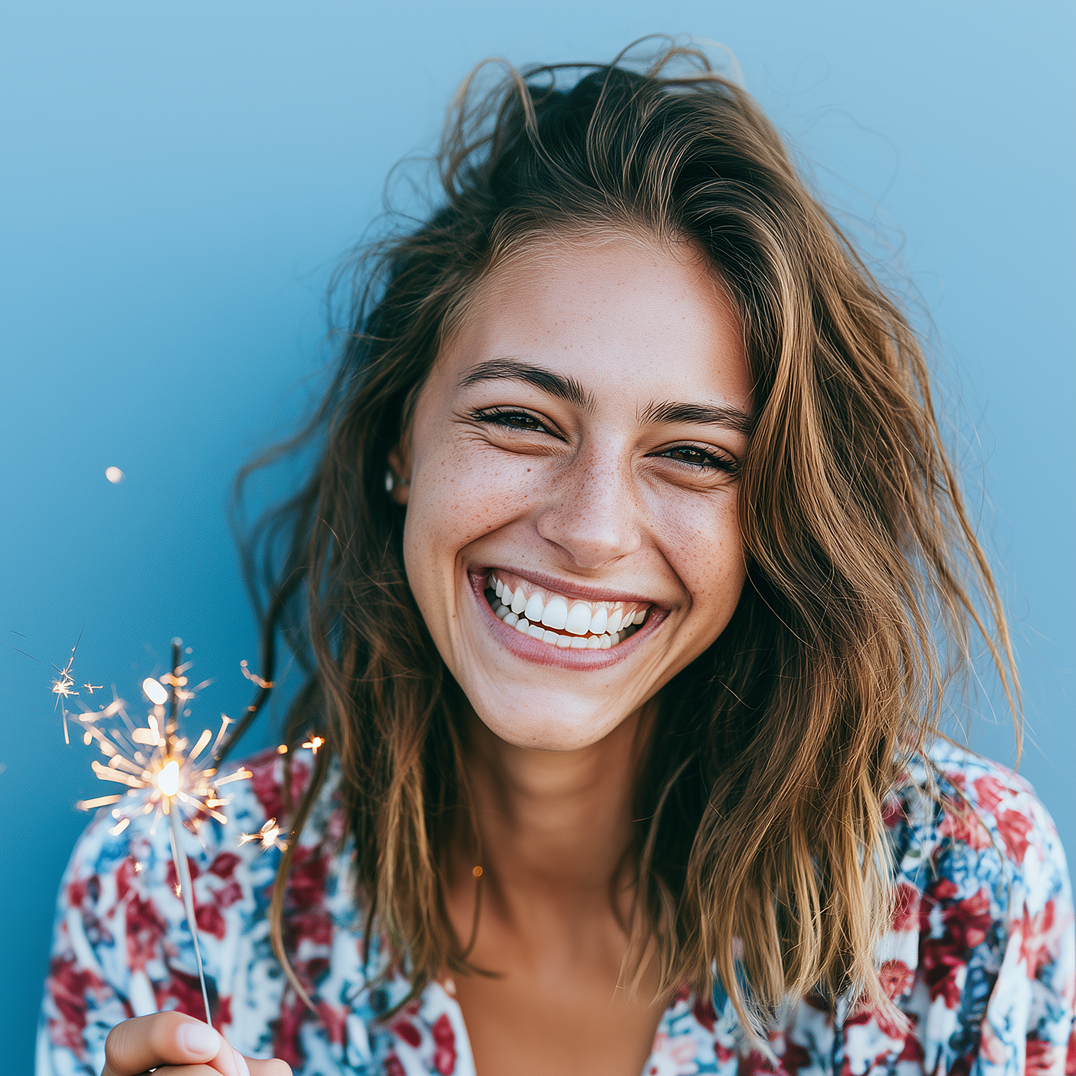Smiling person with messy hair holding a sparkler against a blue background