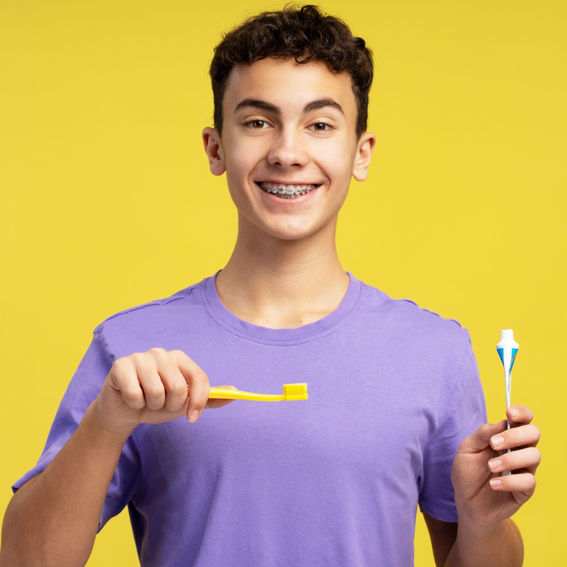 A young man with braces is brushing his teeth with a yellow toothbrush.