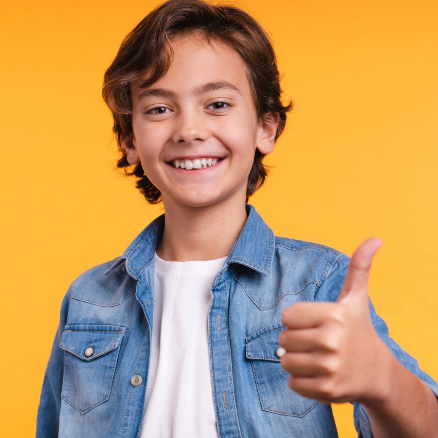 A young boy in a denim shirt is giving a thumbs up