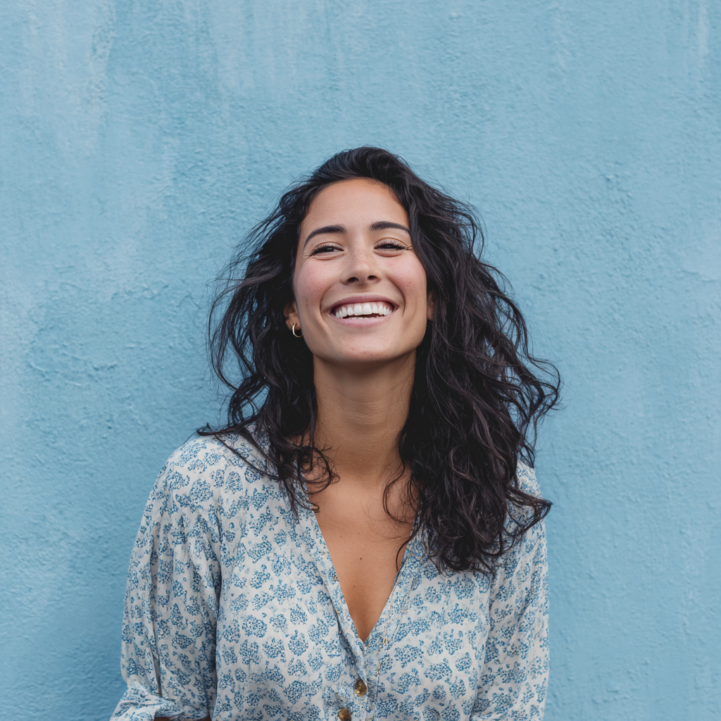 A woman is smiling in front of a blue wall.