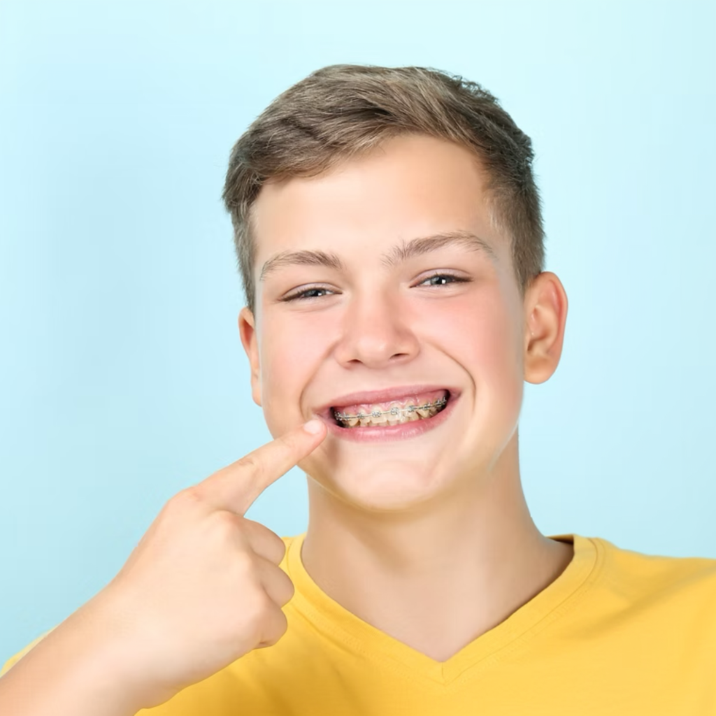 Smiling teen pointing at braces on teeth against a light blue background
