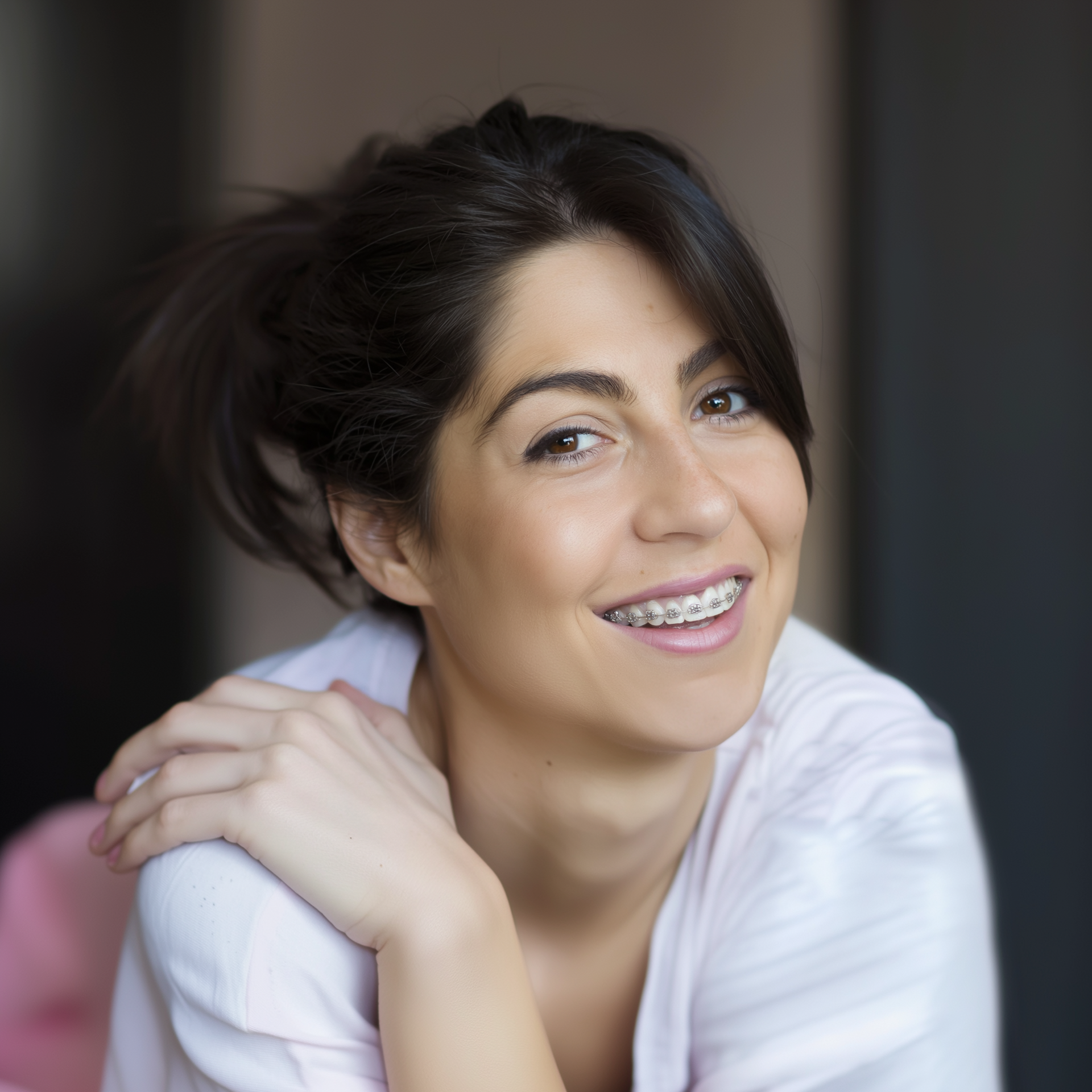 A smiling person with braces, wearing a light pink shirt, posing with a hand resting on their shoulder.