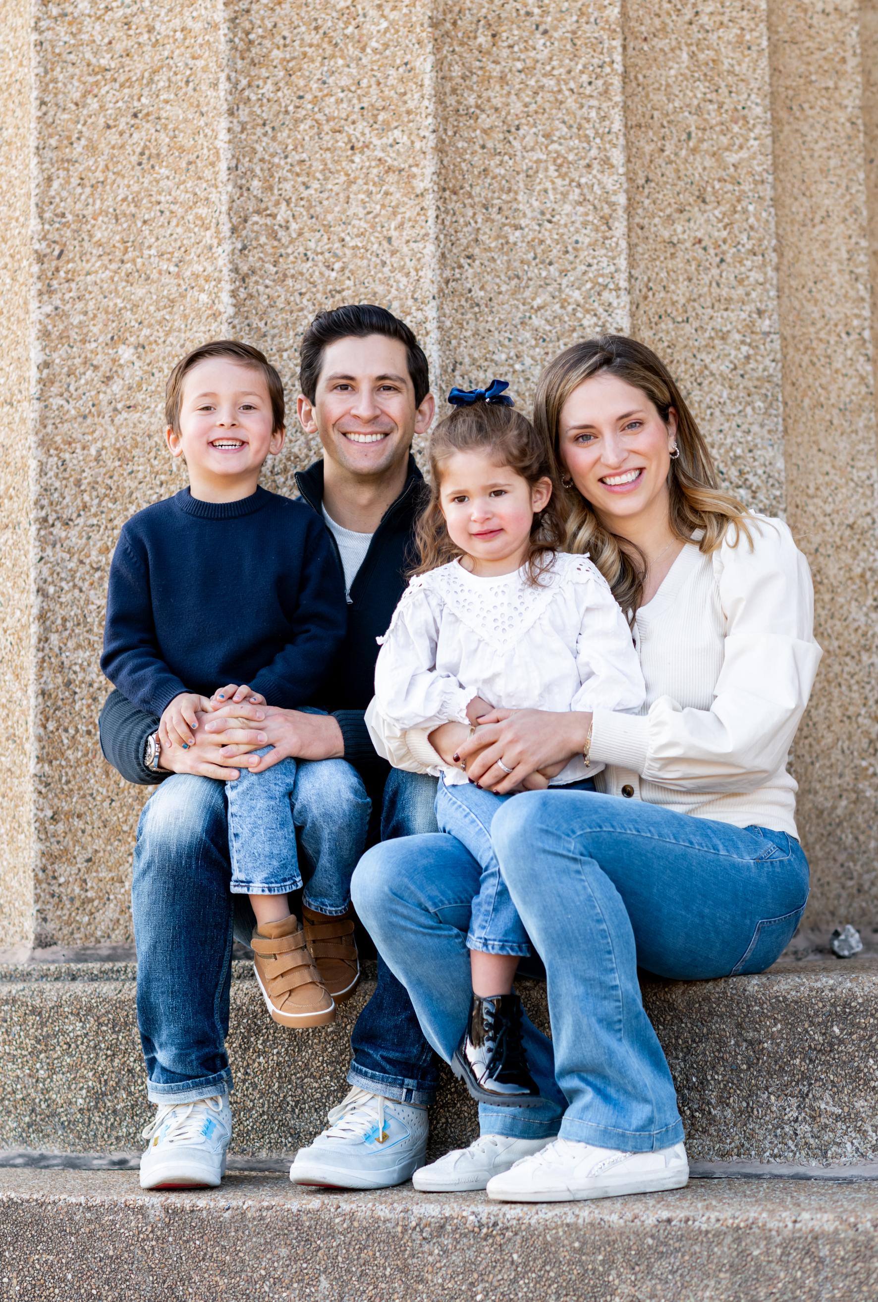 A family is sitting on the steps of a building posing for a picture.