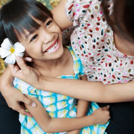 A woman is hugging a little girl with a flower in her hair